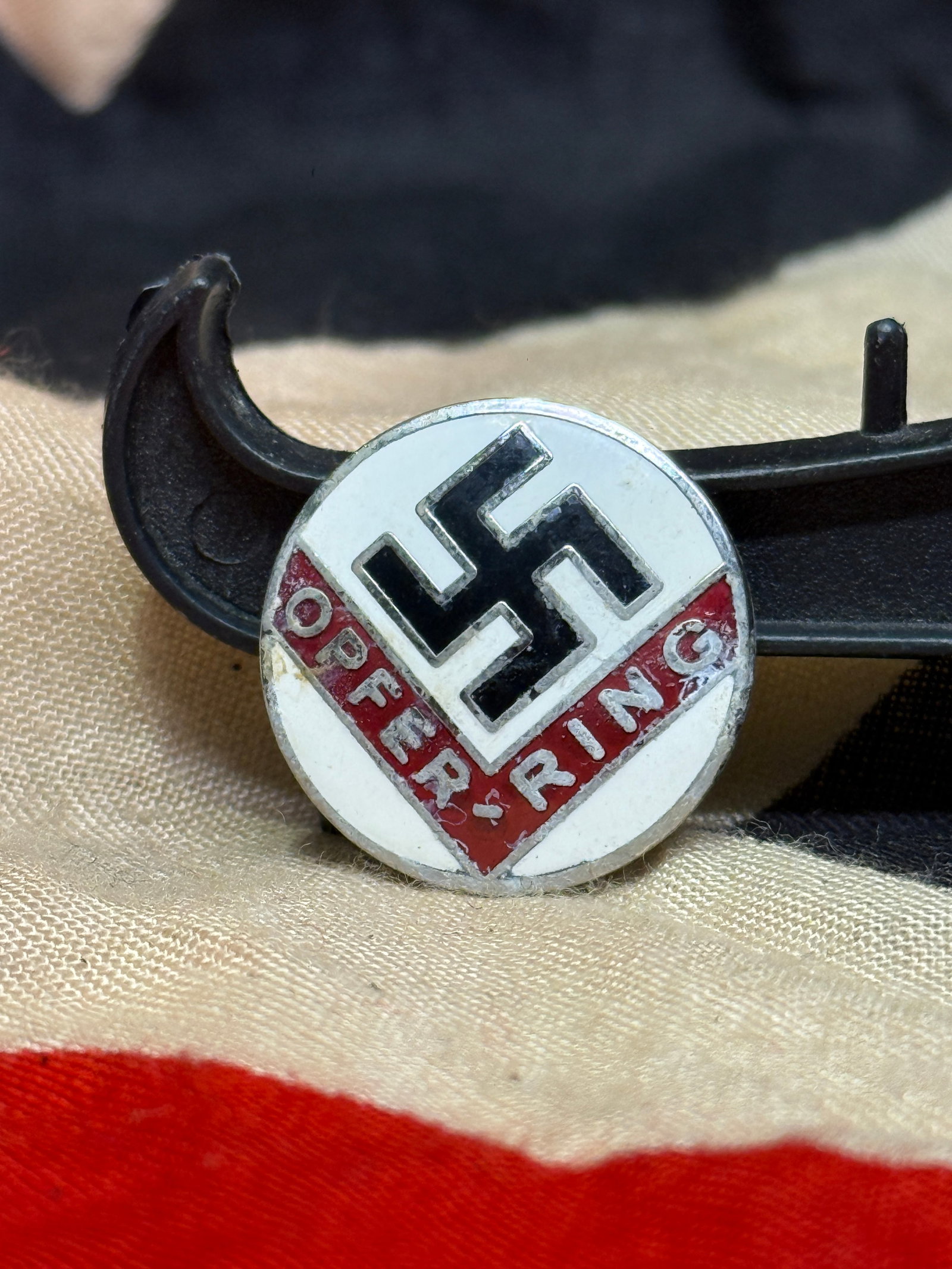 WWII German NSDAP "Opfer Ring" Membership Badge By RZM M1/129: This circular enameled badge features a black swastika against a white field above a red banner inscribed "Opfer Ring" ("Sacrifice Ring"). The reverse retains its original horizontal pin assembly and 