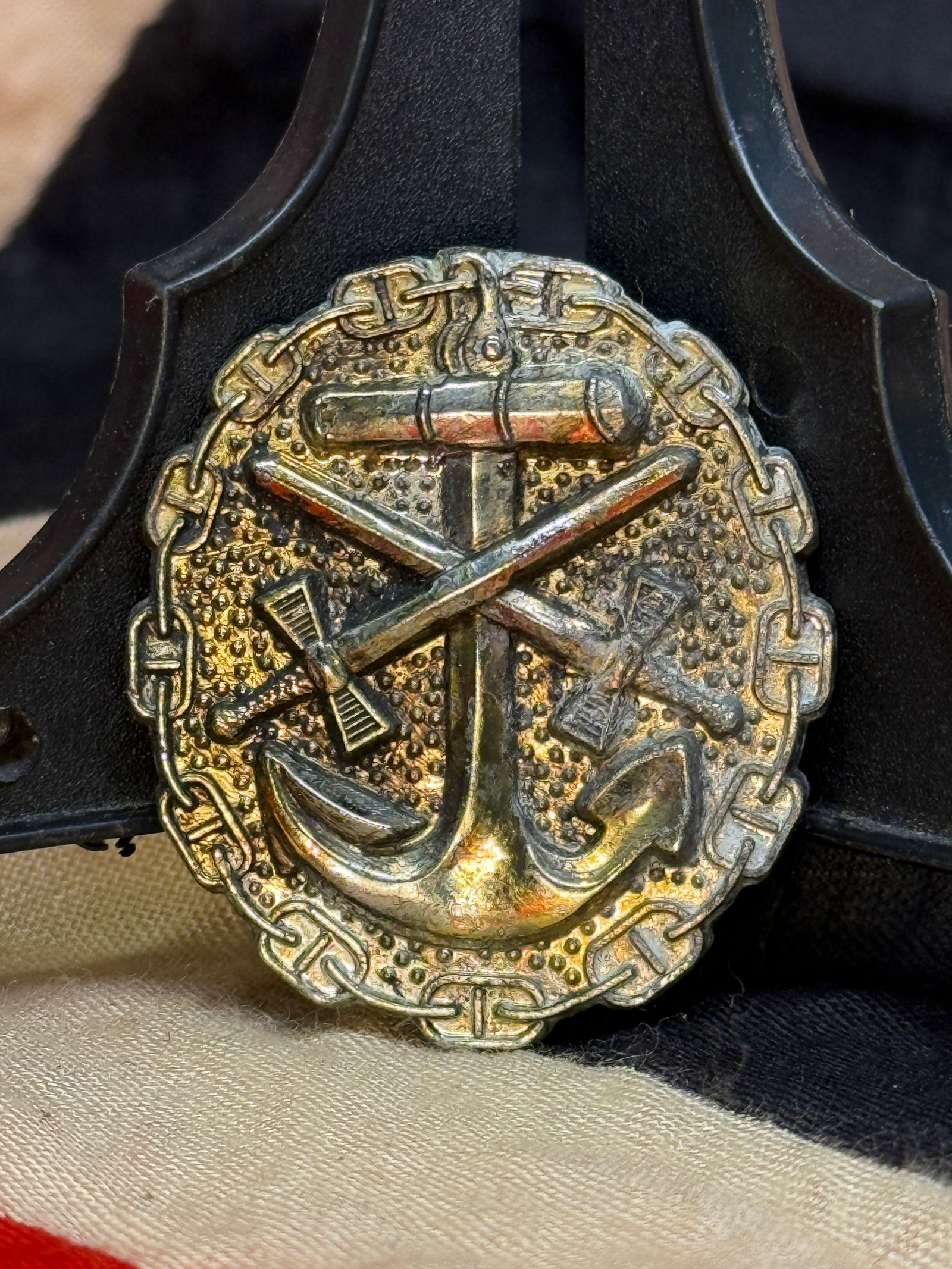 WWII German Kriegsmarine Commemorative Naval Badge: This circular naval badge features a large fouled anchor over crossed maritime and military implements, surrounded by an ornamental chain border. The reverse retains its original vertical pin assembly