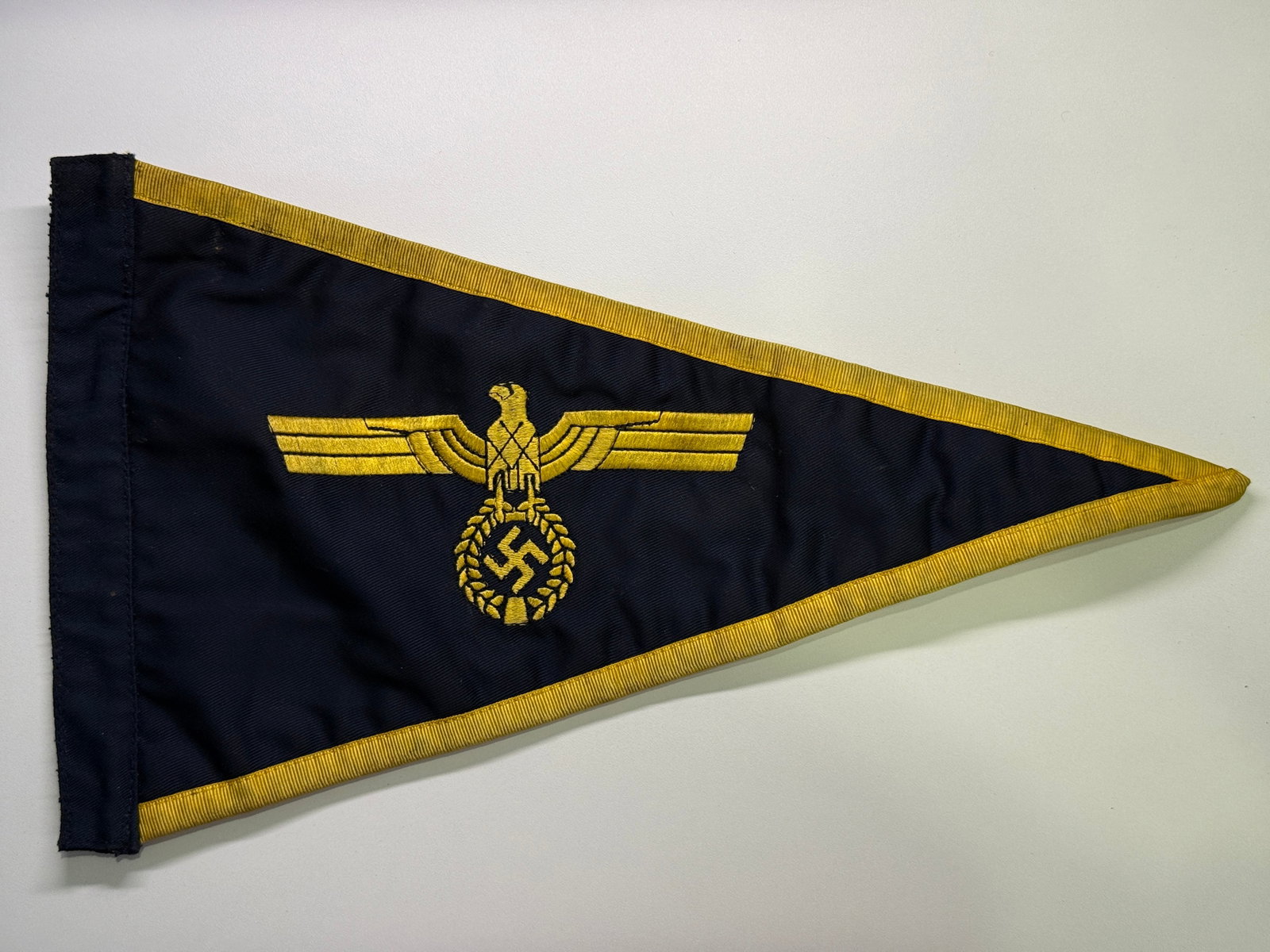 WWII German Kriegsmarine Vehicle Identification Pennant: Double-sided triangular vehicle pennant constructed from dark navy-blue ribbed cloth and bordered on its sloping edges with golden-yellow woven tape. Both faces carry a machine-embroidered golden nati