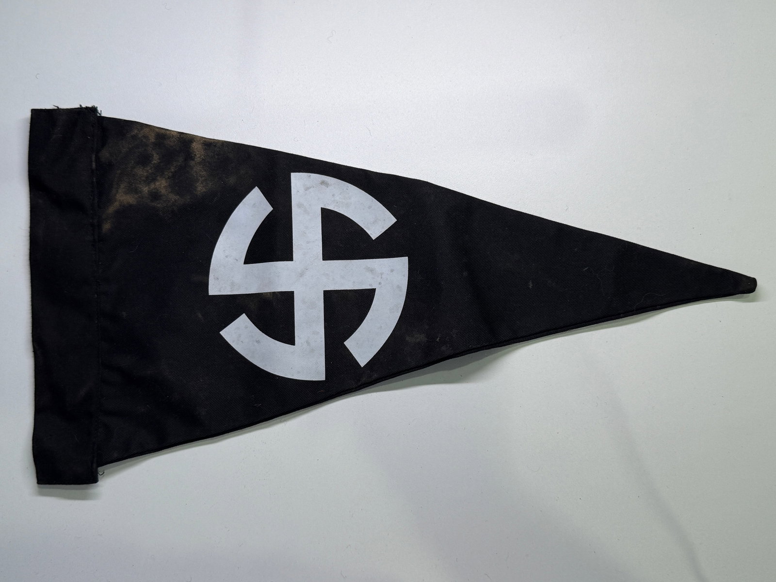 WW2 German Black Political-Symbol Pennant with White Sun-Wheel Device: Double-sided triangular black cloth pennant displaying a large white printed four-armed hooked-cross or sun-wheel device within an implied circular arrangement. A reinforced black sleeve at the hoist 