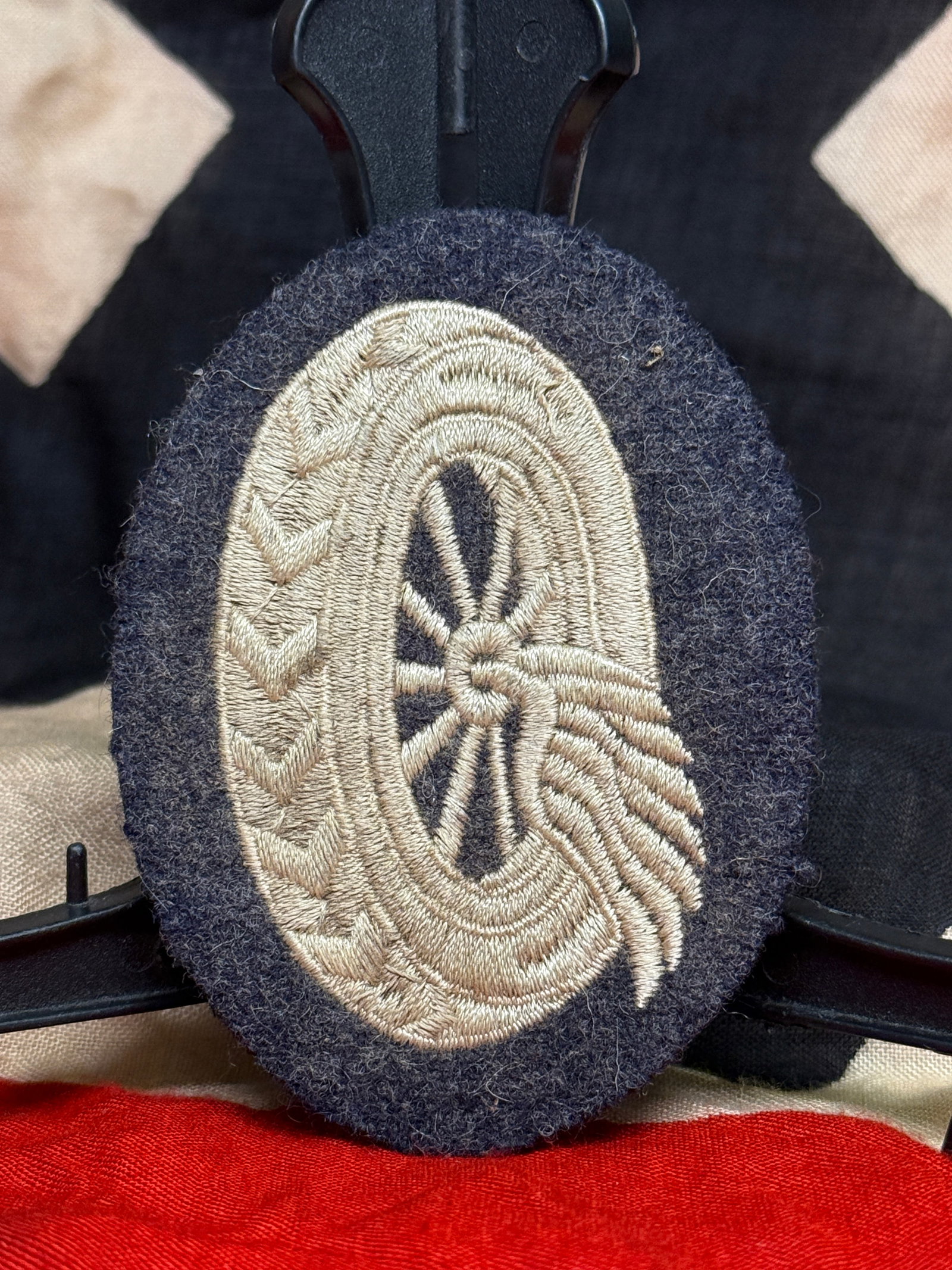 WWII German Luftwaffe Motor Transport Equipment Administrator’s Trade Badge: An embroidered Luftwaffe specialist trade badge for a Kraftfahrzeuggeräteverwalter, or motor-transport equipment administrator. The oval insignia is worked in silver-gray thread on a blue-gray wool b