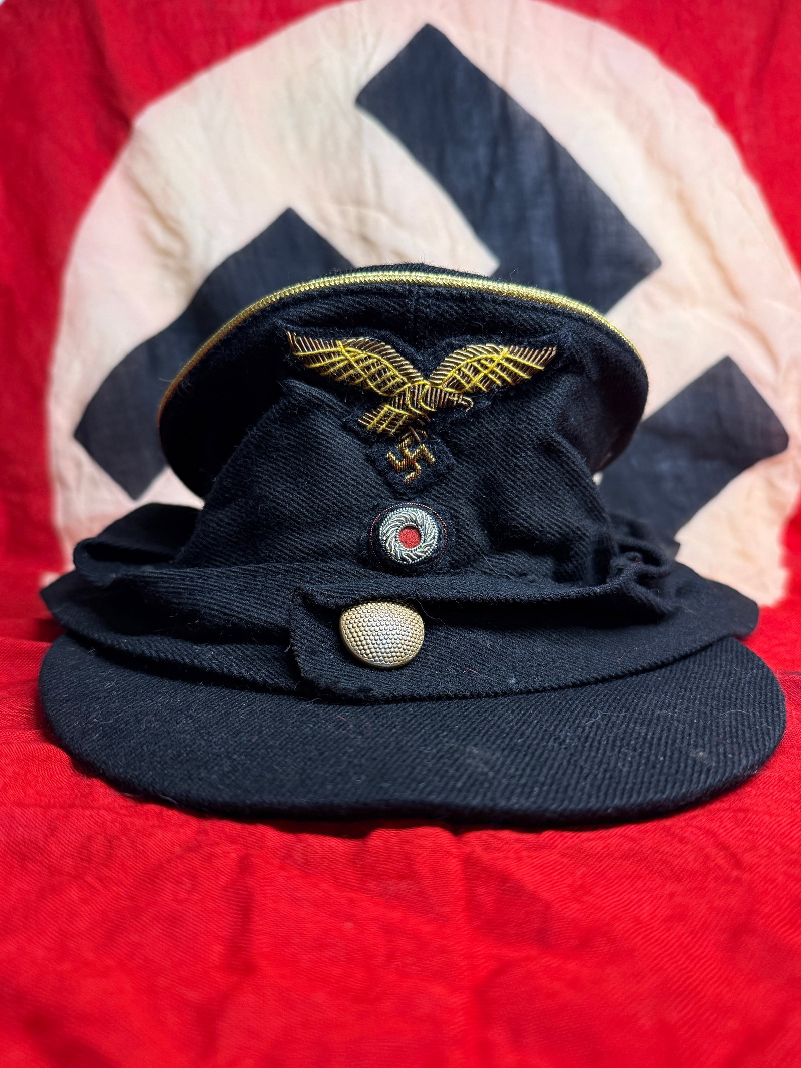 WWII German Kriegsmarine Officer’s Dark-Blue M43 Field Cap, Size 57: A German naval M43 field cap constructed from black or very dark navy wool. The cap has a short cloth-covered visor and a fold-down side and neck panel secured at the front by a single pebbled metal b