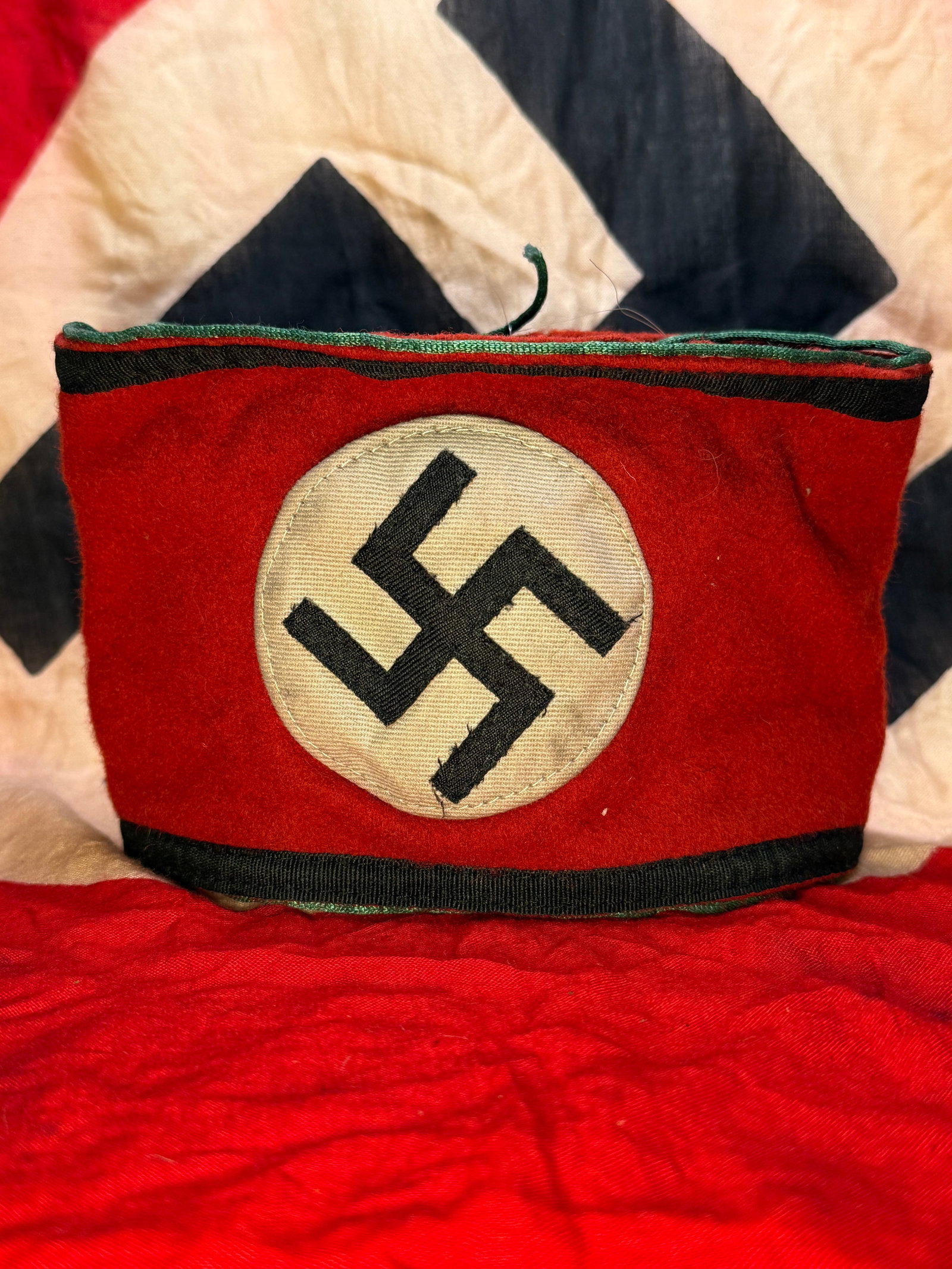 WWII-Era German SS Wool Armband with Black Borders and RZM/SS Label: A red wool SS service armband centered by a white circular cloth field bearing a separately applied black swastika. Black woven bands border the upper and lower edges, distinguishing the SS pattern fr