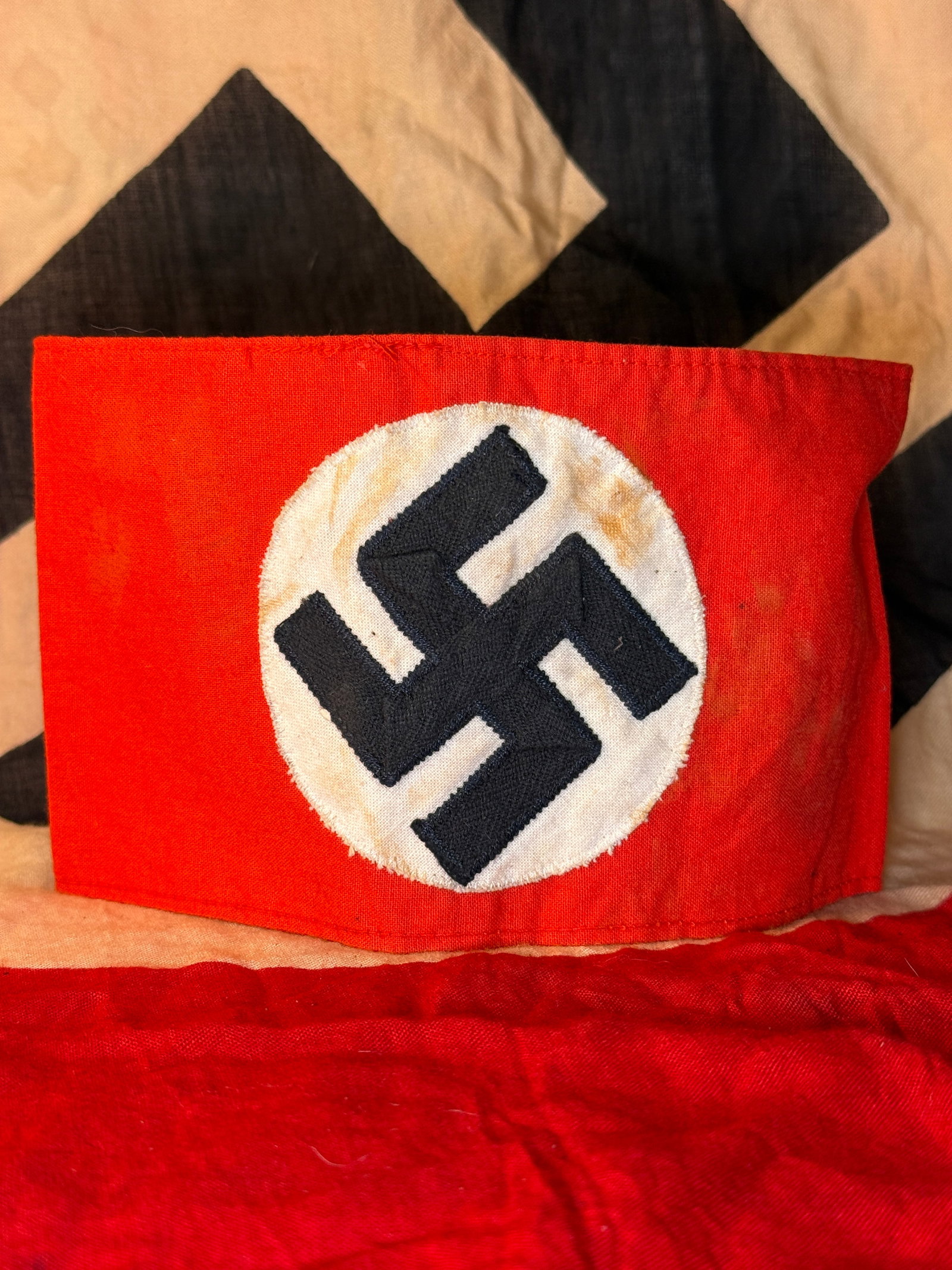 WWII German NSDAP Party Member Armband: Red cloth National Socialist German Workers’ Party armband with a centrally applied white circular field and black embroidered swastika. The armband is assembled as a closed sleeve with machine-stit