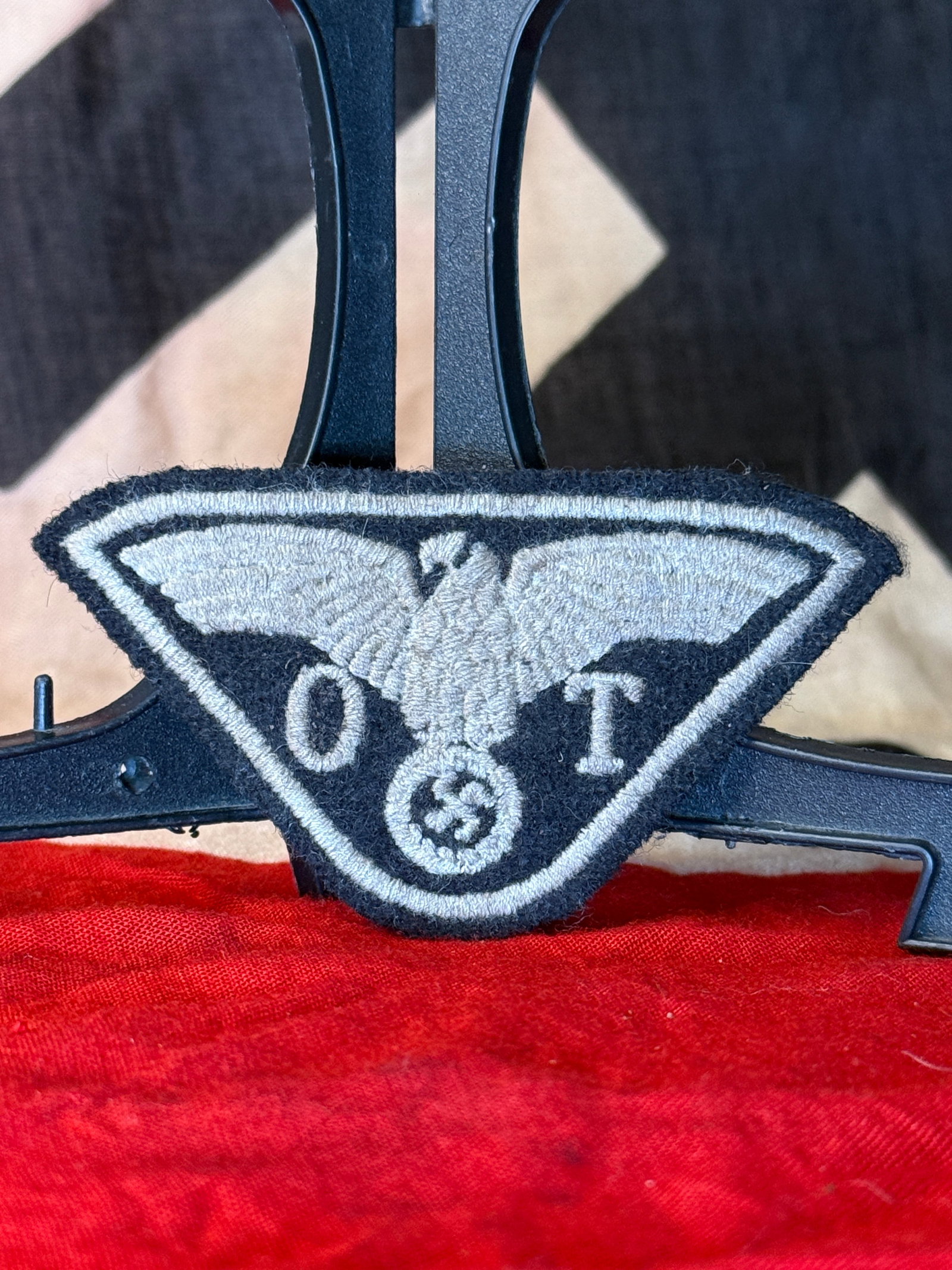 WWII German Organisation Todt (OT) Embroidered Sleeve Badge: Triangular black wool insignia embroidered in silver-grey thread with the Organisation Todt emblem: a spread-winged eagle positioned above a wreathed swastika and flanked by the letters “O” an