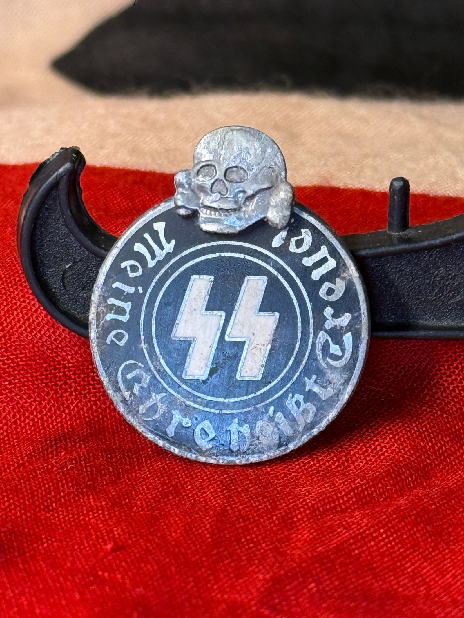 WWII-Era German SS-Motif “Meine Ehre heißt Treue?? Badge, RZM M1/42 Marked: Oval metal badge with a black central field, silver-colored border and raised skull-and-crossbones ornament positioned above the body. The center displays the double lightning-bolt runes associated wi