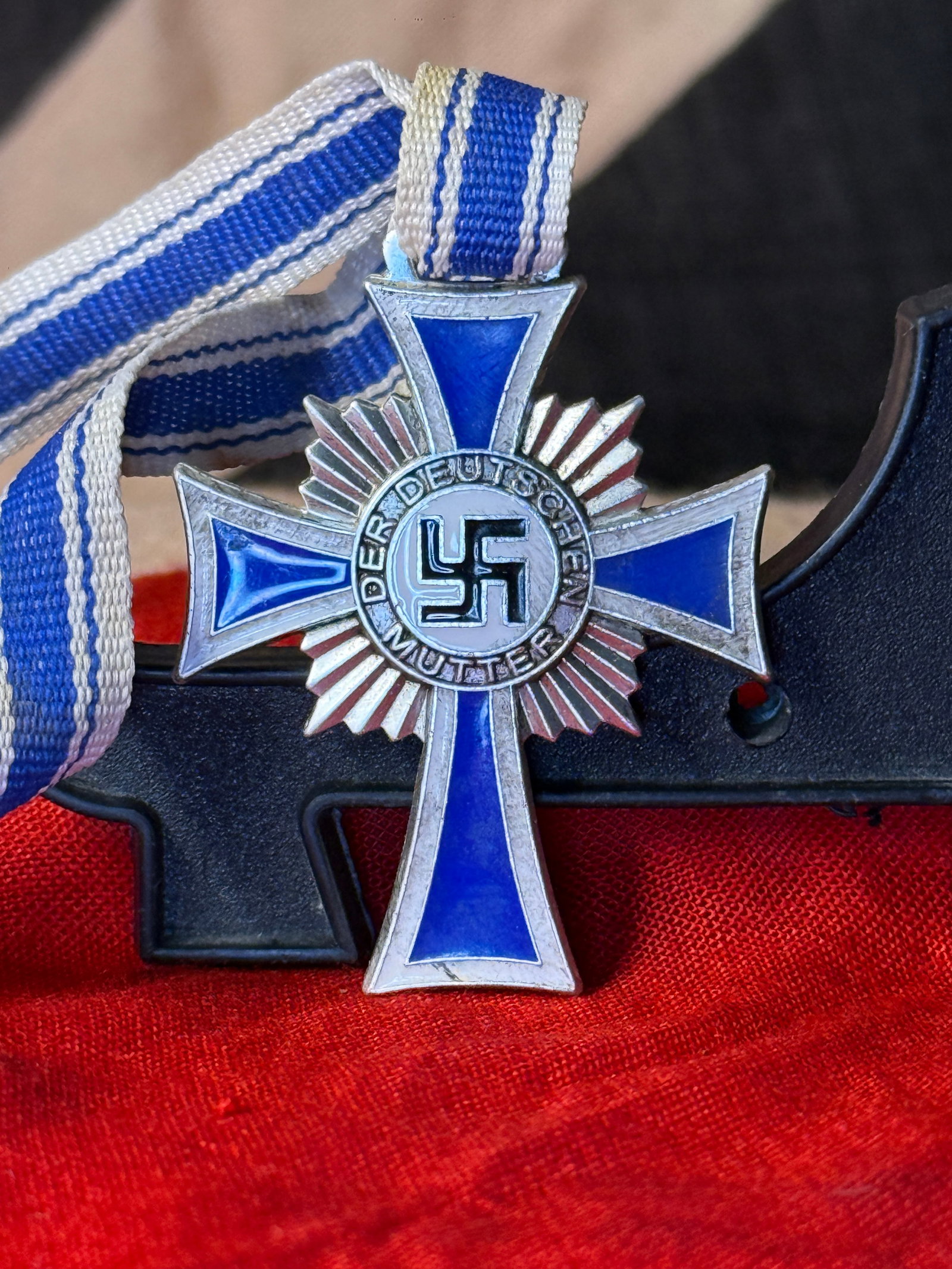 WWII German Mother’s Cross in Silver — Ehrenkreuz der Deutschen Mutter, Instituted 1938: Silver-grade Cross of Honor of the German Mother, constructed as an elongated cross with blue enamel panels, white borders and radiating silver-colored rays between the arms. Its central white medalli