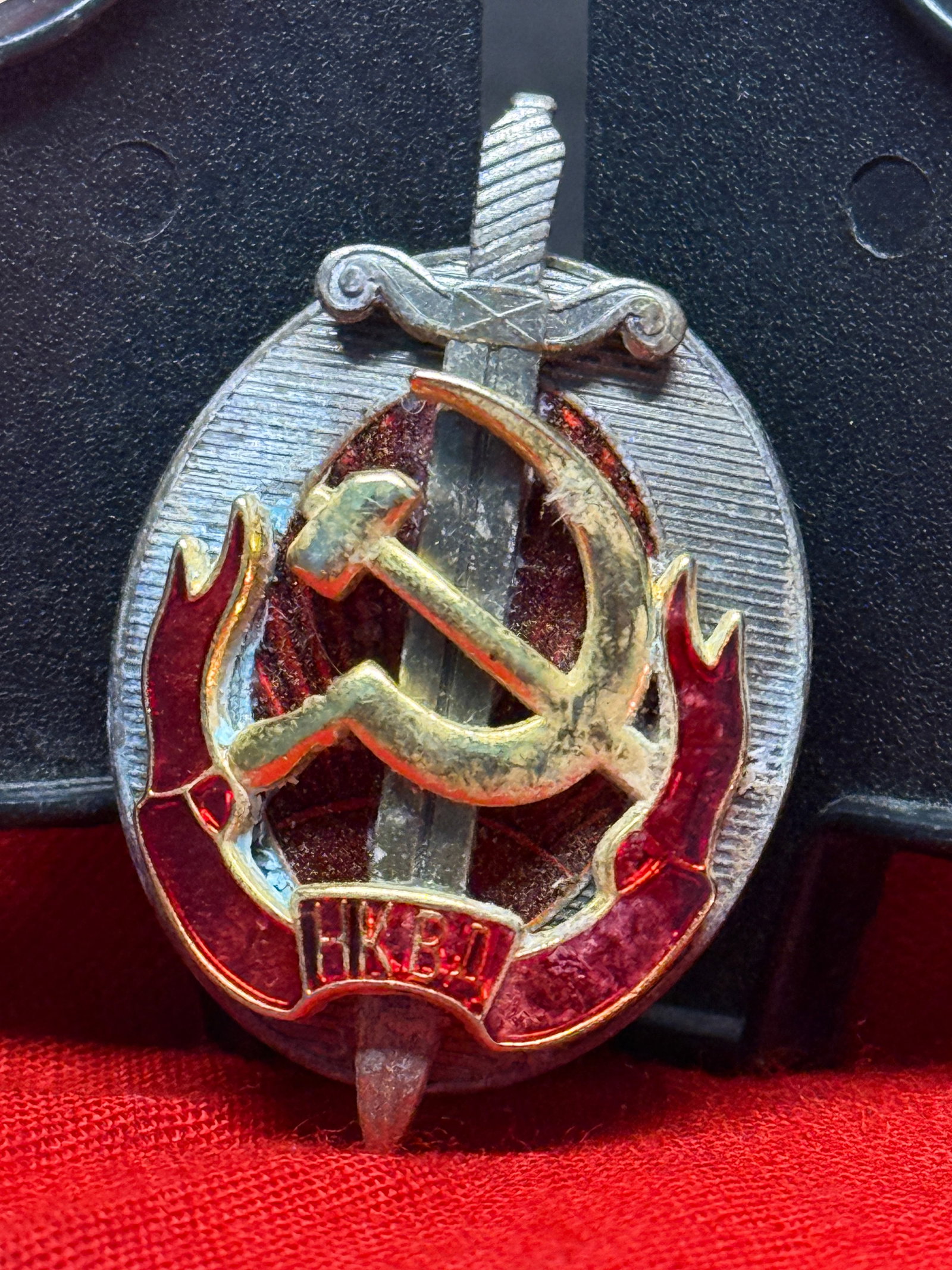 WWII-Era USSR NKVD “Honored Worker?? Badge: Oval Soviet NKVD award badge featuring a gilt hammer-and-sickle over a vertical sword, framed by red enamel flame motifs and a radiating silver-toned field. The lower cartouche bears the Cyrillic init