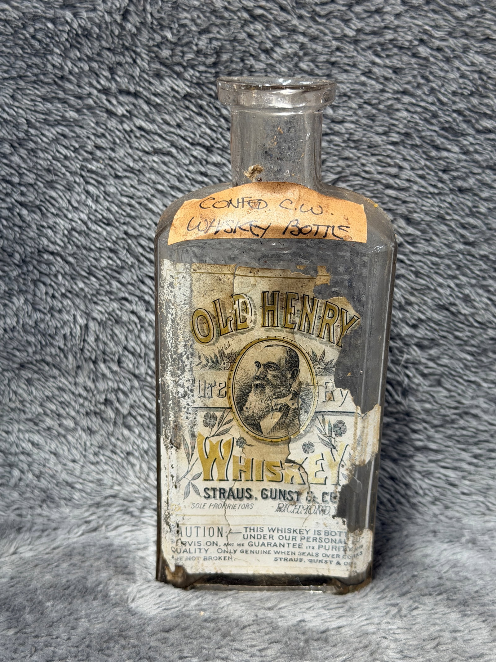 Old Henry Whiskey Bottle Straus Gunst & Co Richmond VA Confederate Civil War Relic: Offered here is an early clear glass “Old Henry Whiskey” bottle bearing a substantial portion of its decorative paper label. The label features a portrait at center surrounded by floral decora