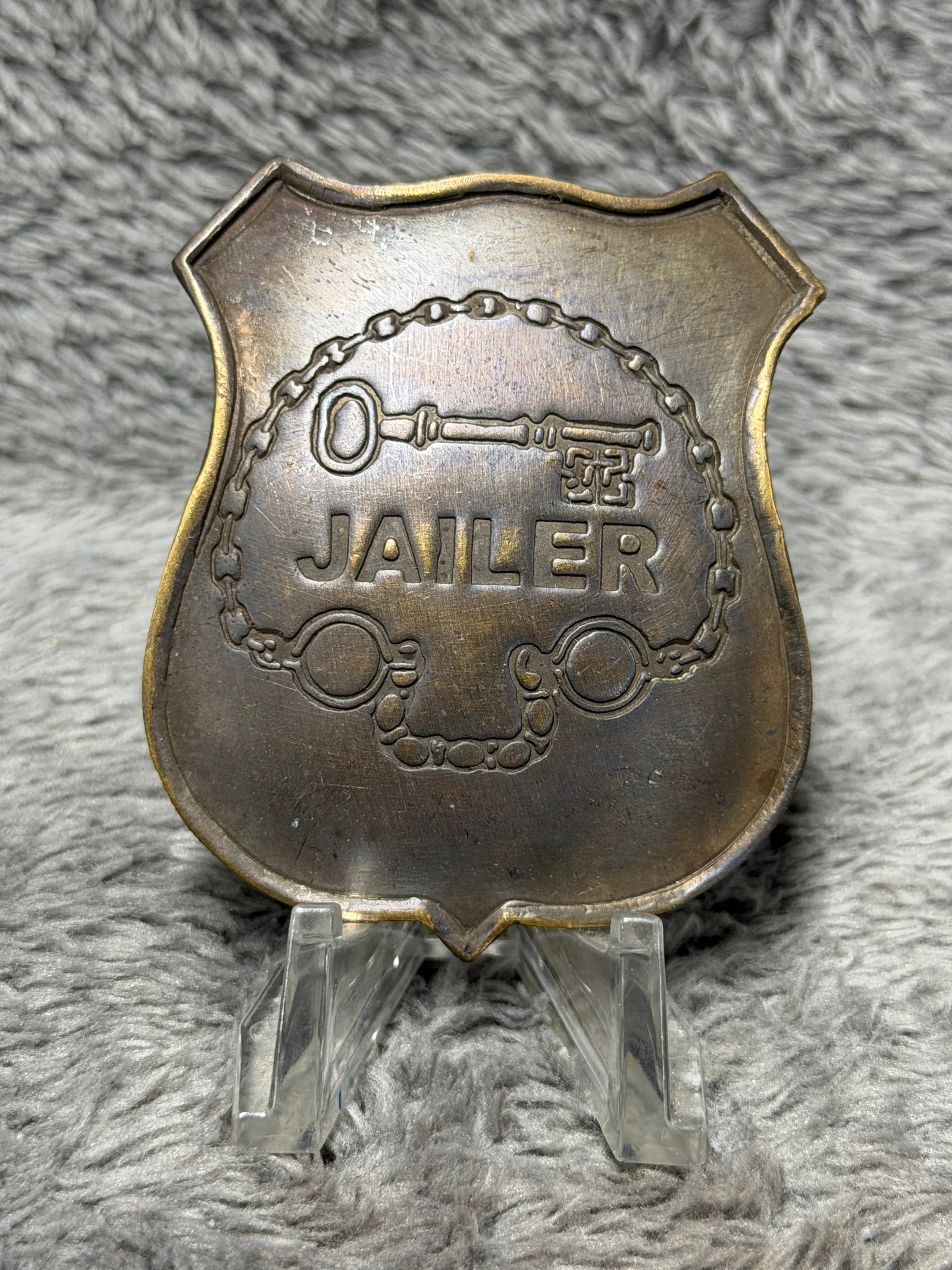Jailer Badge Shield Key & Shackles Design Prison Guard Law Enforcement: Offered here is a shield-shaped metal badge prominently marked “JAILER” across the center. The face features a raised skeleton key above the lettering together with a detailed chain and shackl