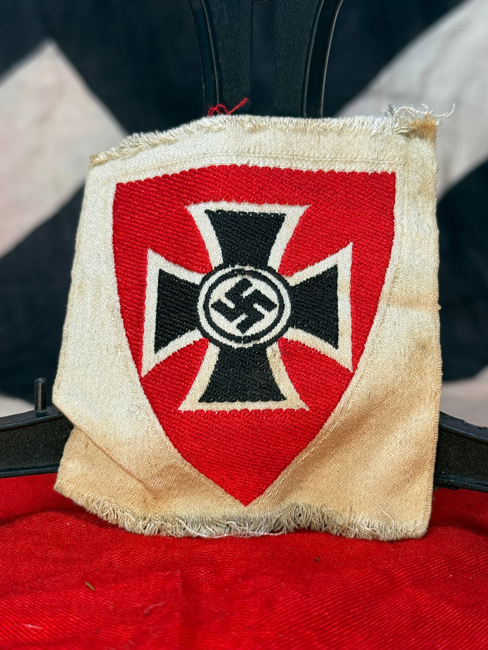 WWII German National Socialist War Victim's Care (NSKOV) Sleeve Shield: This embroidered cloth sleeve shield features the distinctive black cross with central swastika displayed on a red shield against a white field. Sleeve shields of this pattern were worn by members of 