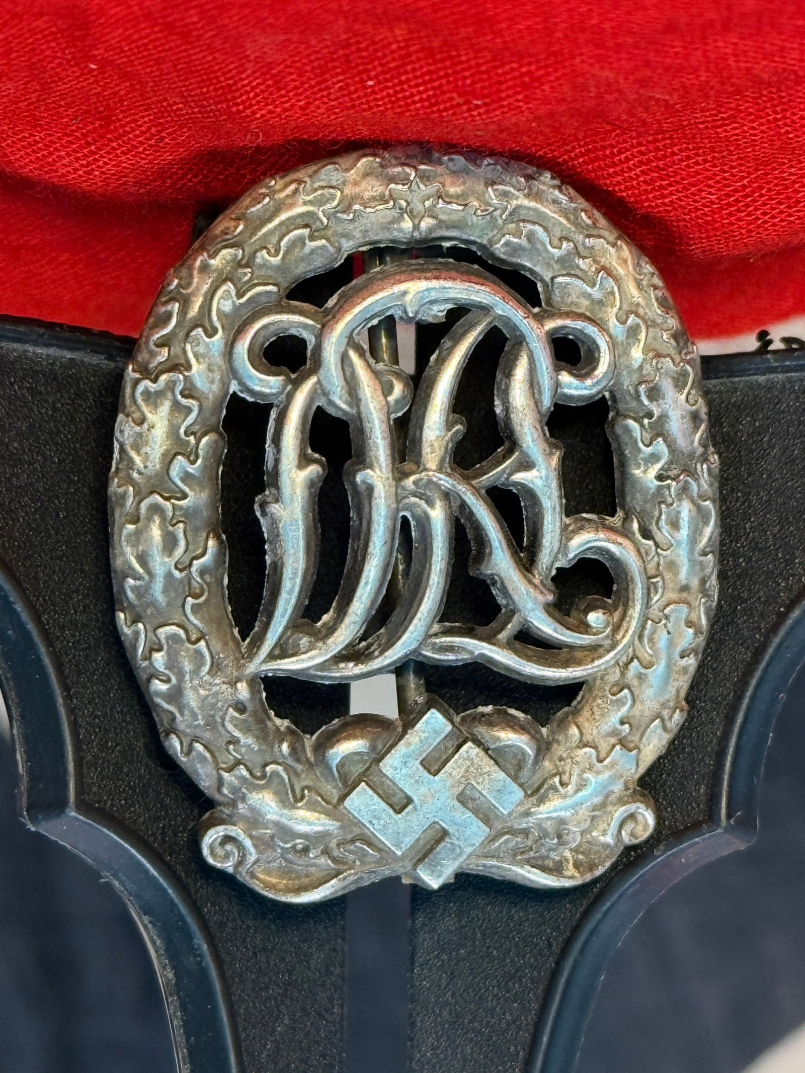 WWII German DRL Sports Badge in Silver: This Deutsches Reichssportabzeichen (DRL) Sports Badge features the intertwined DRL monogram within an oak leaf wreath surmounted by a swastika. The reverse retains its original vertical pinback assem