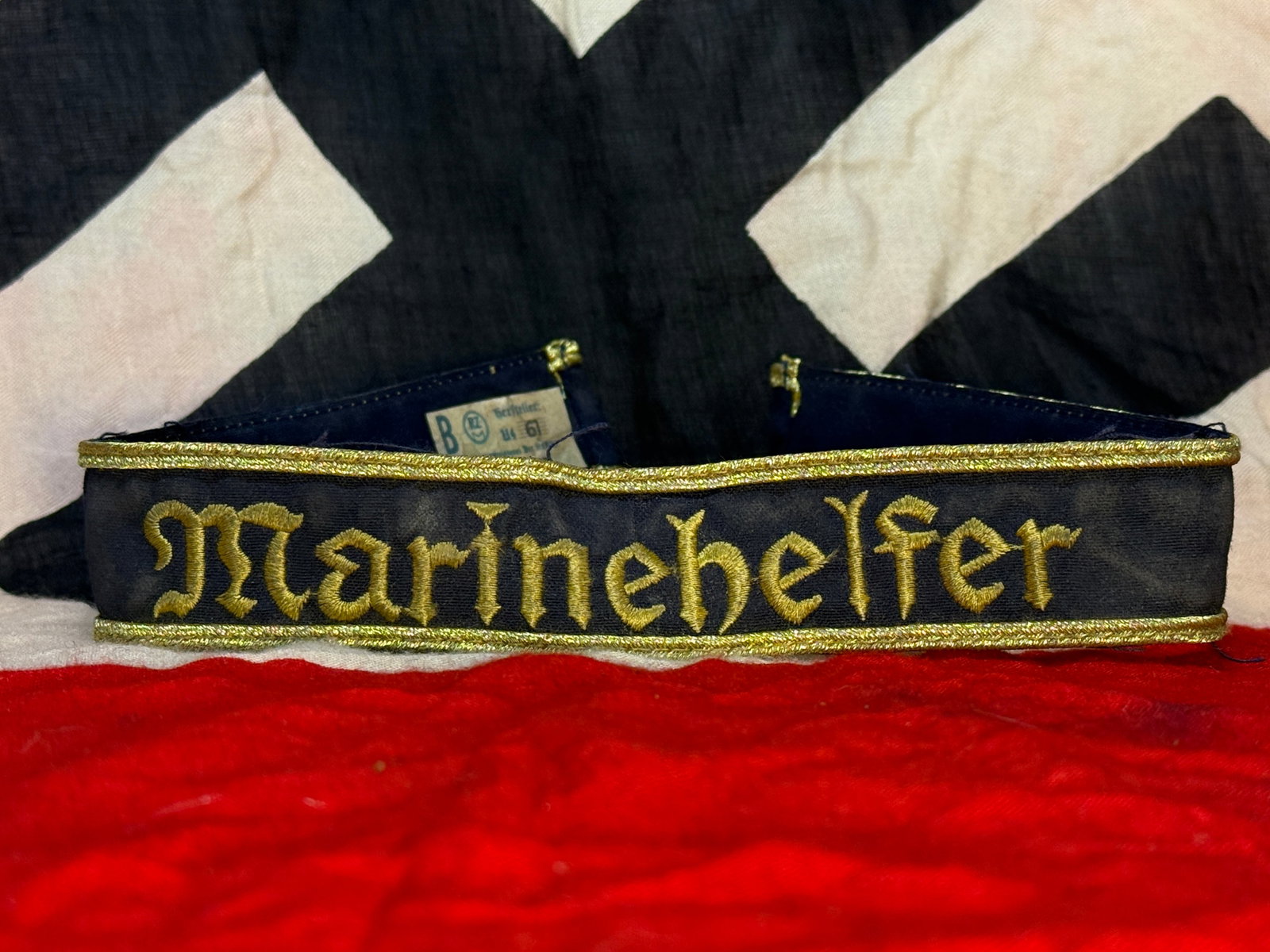 WWII German Marine-HJ (Hitler Youth Naval Auxiliary) "Marinehelfer" Cuff Title: This dark blue cuff title is embroidered in gold Gothic script with the word "Marinehelfer," identifying it as a cuff title worn by members of the Marine-HJ (Hitler Youth Naval Auxiliary) during World