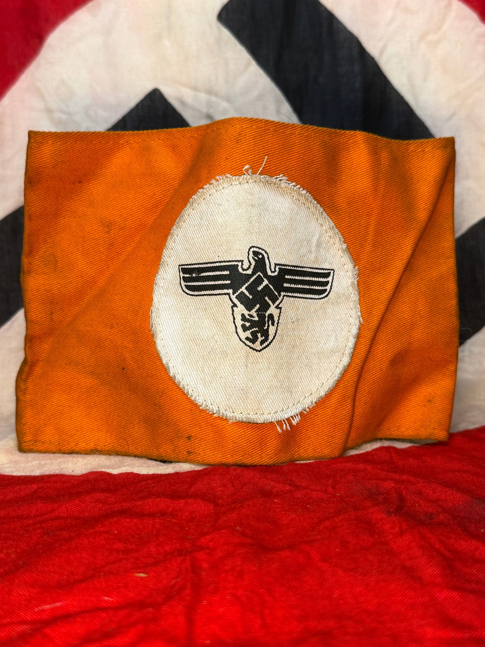 WWII German State Service (Staatsdienst) Armband: This orange cloth armband features a white oval panel printed with the German national eagle above a swastika, identifying it as a State Service (Staatsdienst) armband worn by civilian government pers