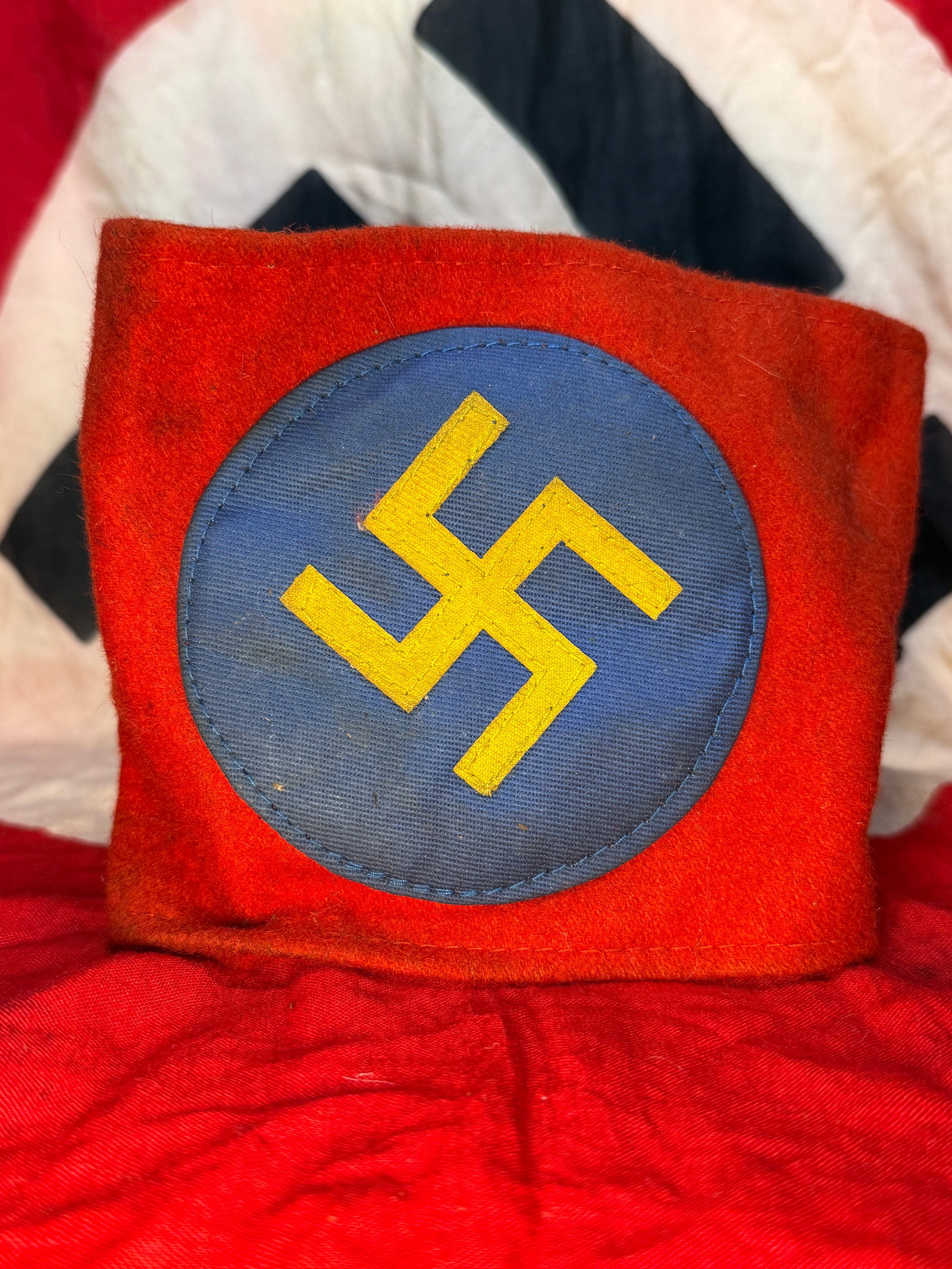 WWII German NSDAP Political Leader Armband: This red wool armband features a separately applied blue roundel with a gold swastika at its center, a distinctive pattern associated with political leadership within the National Socialist German Wor