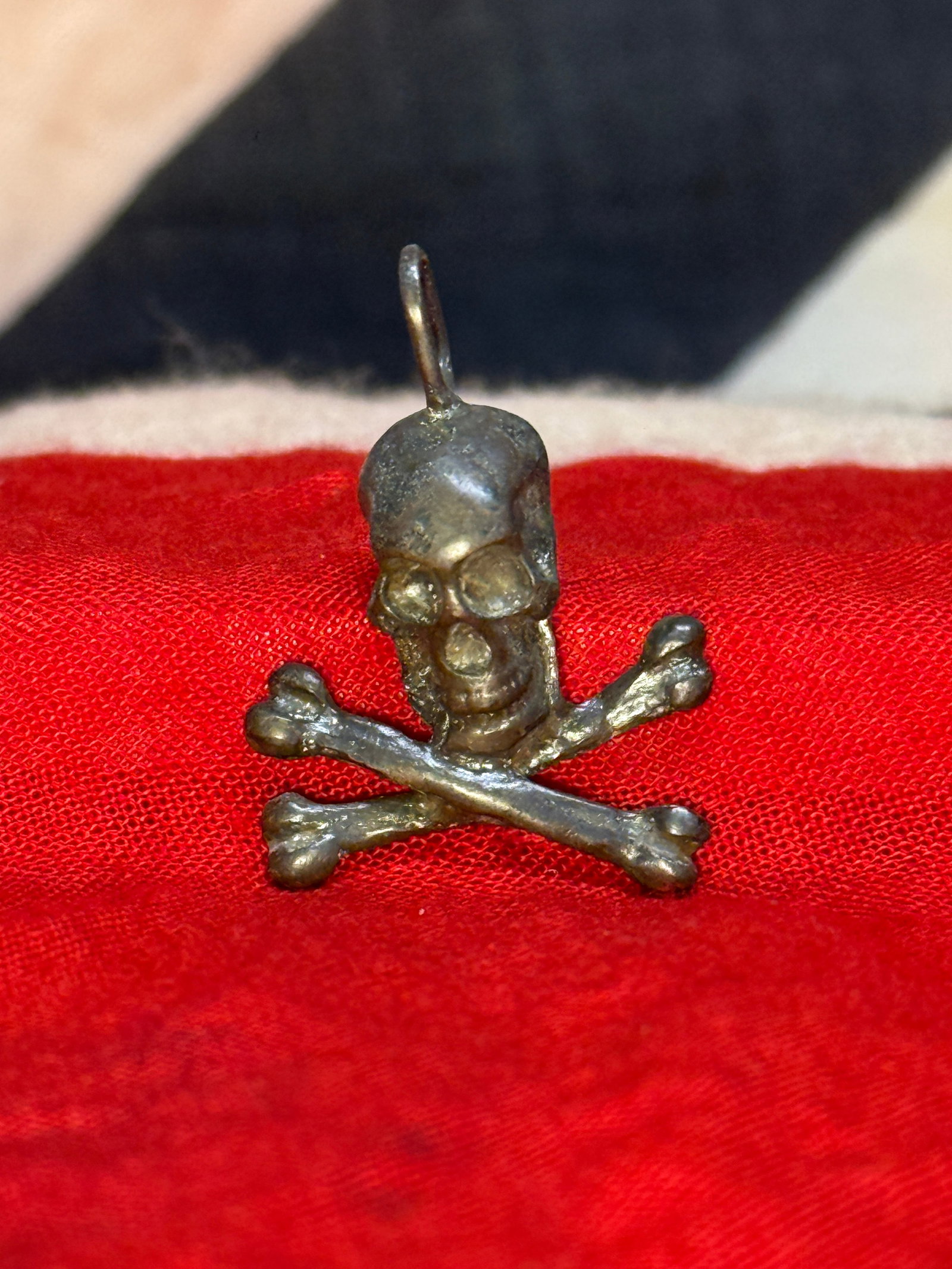 WWII German SS Totenkopf Skull and Crossbones Pendant: This cast metal pendant depicts the iconic Totenkopf, featuring a skull above crossed bones with an integral suspension loop for wear as a personal charm or pendant. The Totenkopf became one of the mo
