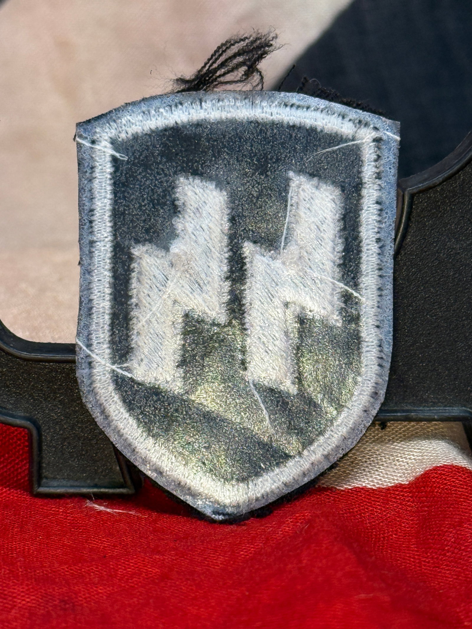 WWII German Waffen-SS Sleeve Insignia Patch: This embroidered cloth sleeve insignia features the iconic dual SS runes in silver-gray thread on a black shield-shaped backing with a matching embroidered border. The SS runes served as one of the pr