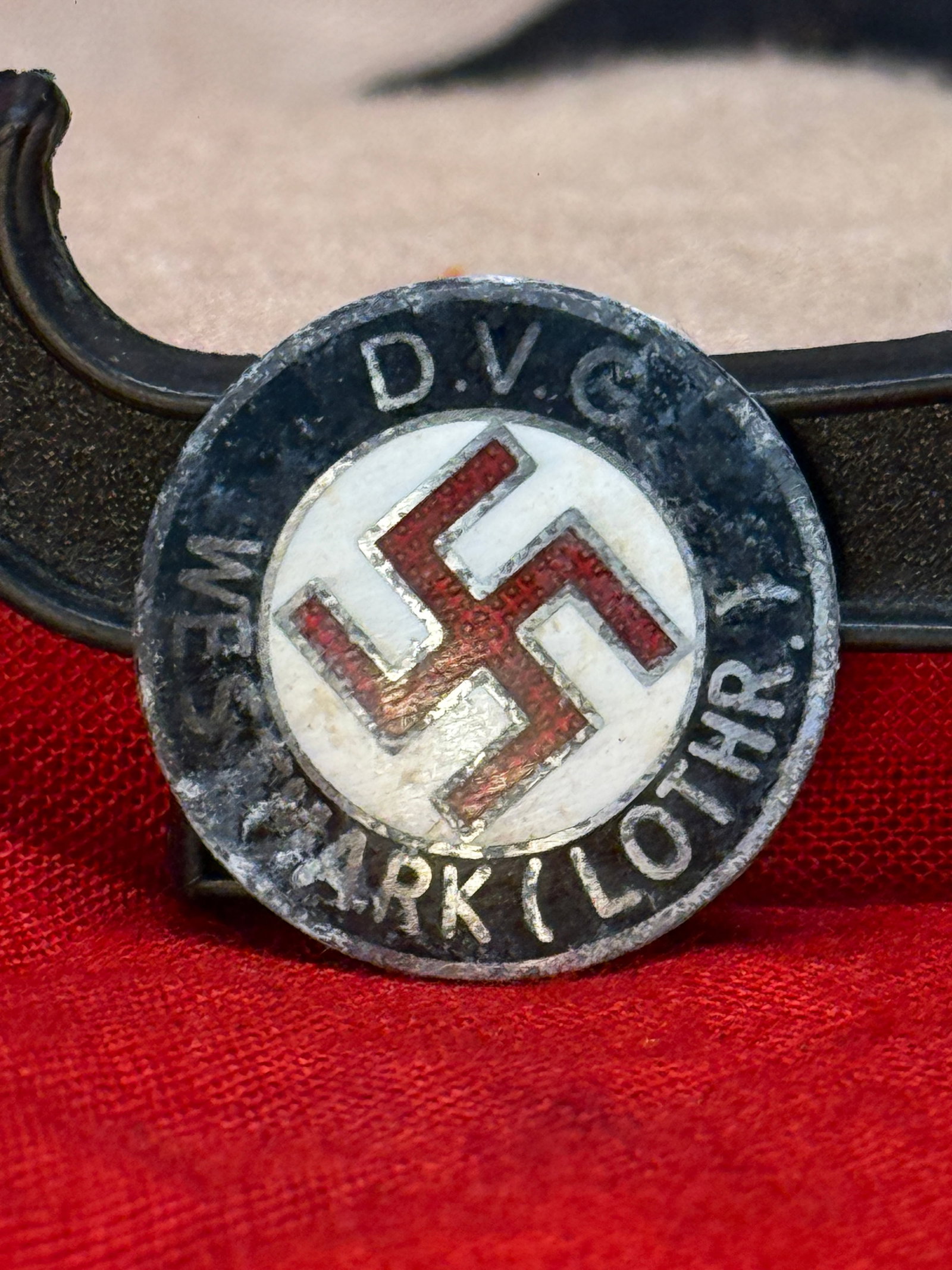 WWII German Deutsche Volksgemeinschaft (D.V.G.) Membership Badge: This circular enamel membership badge displays a red swastika within a white center encircled by the inscription "D.V.G. WESTMARK (LOTHR.)" The reverse retains its original horizontal pinback assembly