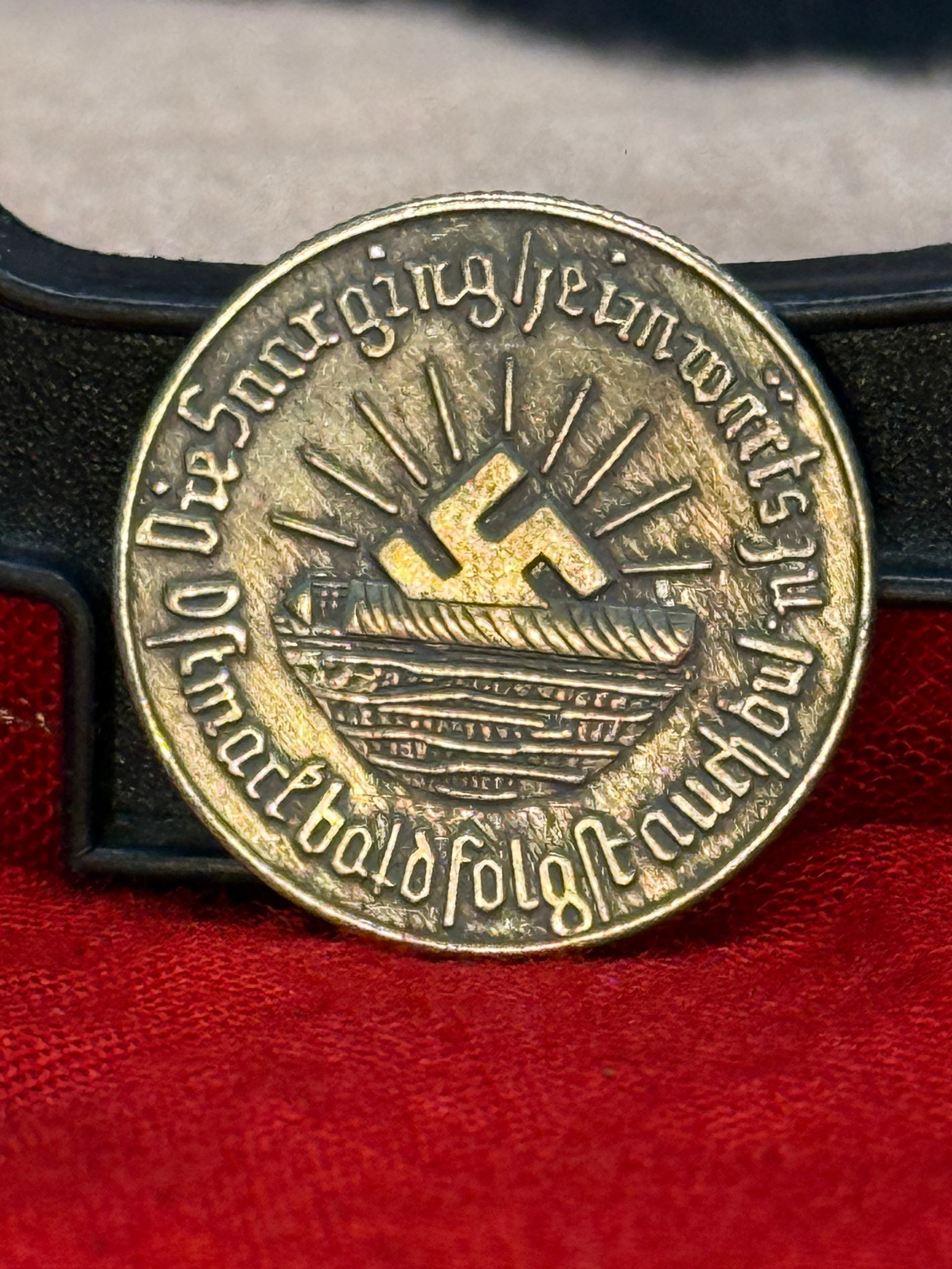 WWII German SA “Ein Schilling?? Winter Relief / Gau Mark Brandenburg Token: WWII-era German round metal token featuring a prominent SA emblem on one side with the inscription “EIN SCHILLING.” The opposite side displays a stylized ship beneath a swastika and radiating 