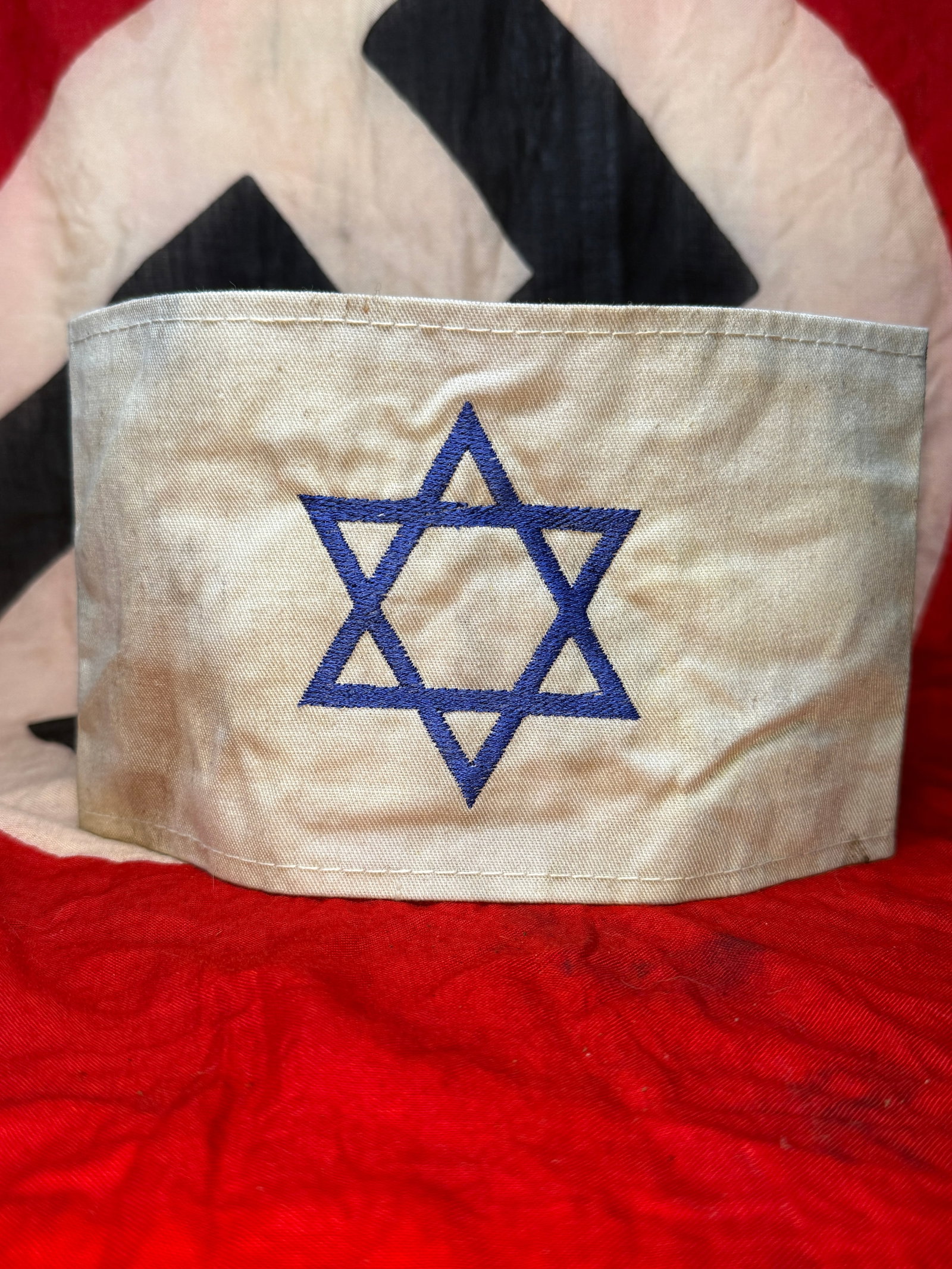 WWII German Jewish Identification Armband: This white cotton identification armband features a blue embroidered Star of David, the symbol that Jewish civilians were required to wear under Nazi rule during the Second World War. The armband is c