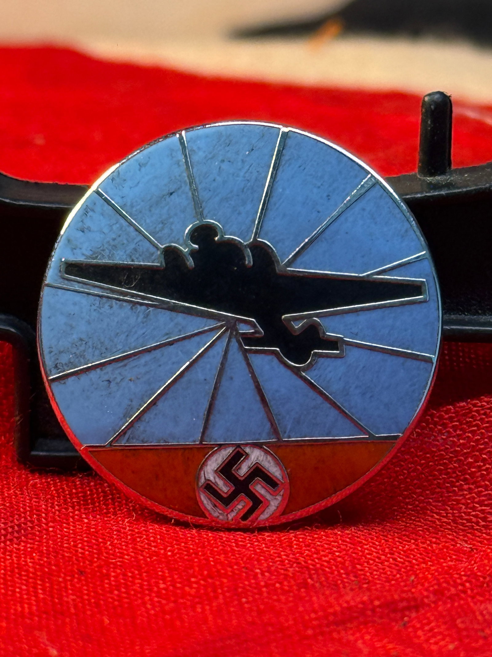 WWII German Aircraft Reporting Service Membership Badge: This circular enameled membership badge depicts the silhouette of a twin-engine aircraft flying across blue radiating rays above a swastika emblem. The reverse retains its original pin assembly and is