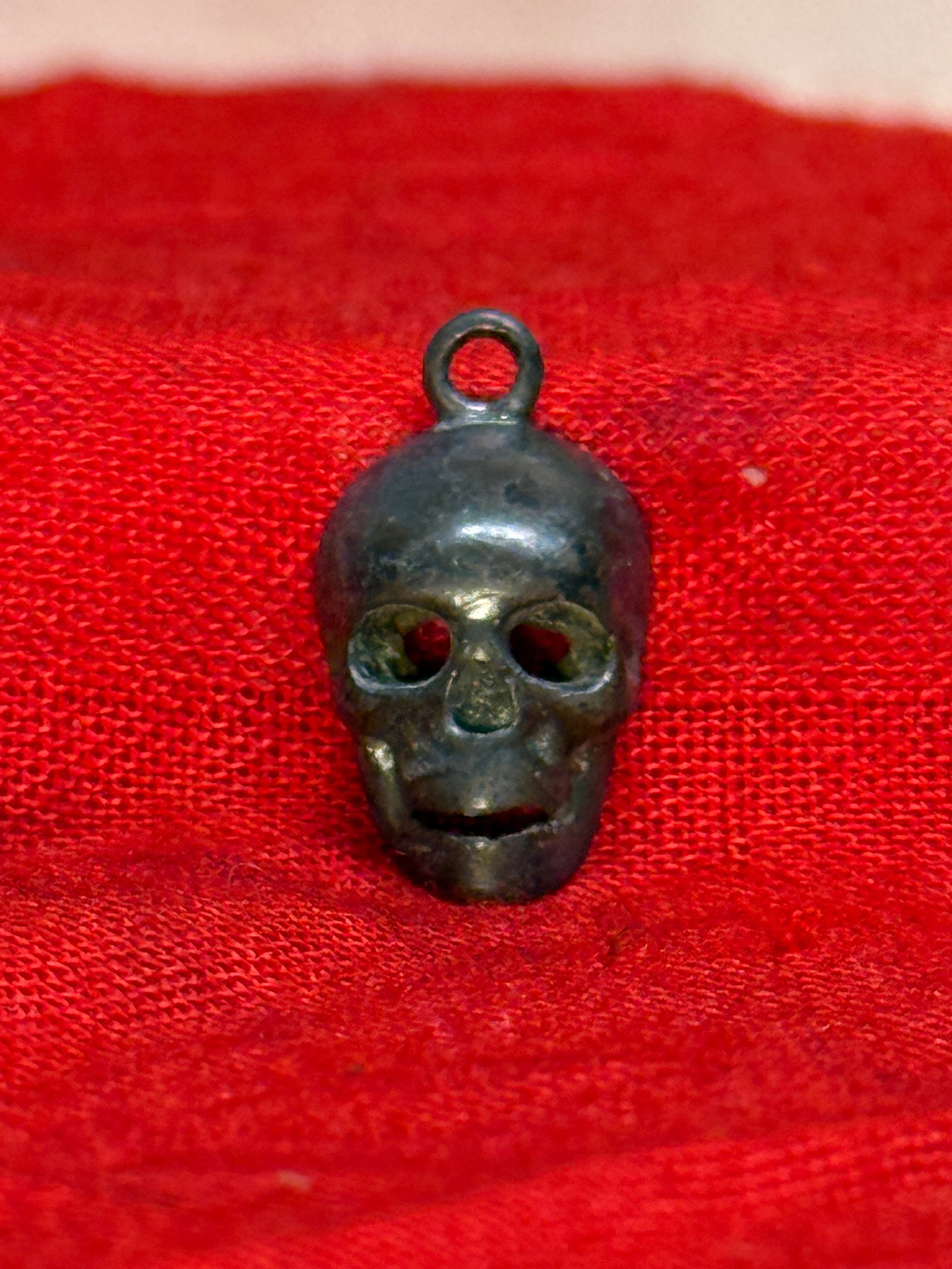 WWII German SS Totenkopf Skull Silver Pendant: This small cast metal pendant depicts a stylized Totenkopf (Death's Head) with hollow eye sockets and an integral suspension loop for wear as a pendant or charm. The reverse is hollow cast, reflecting
