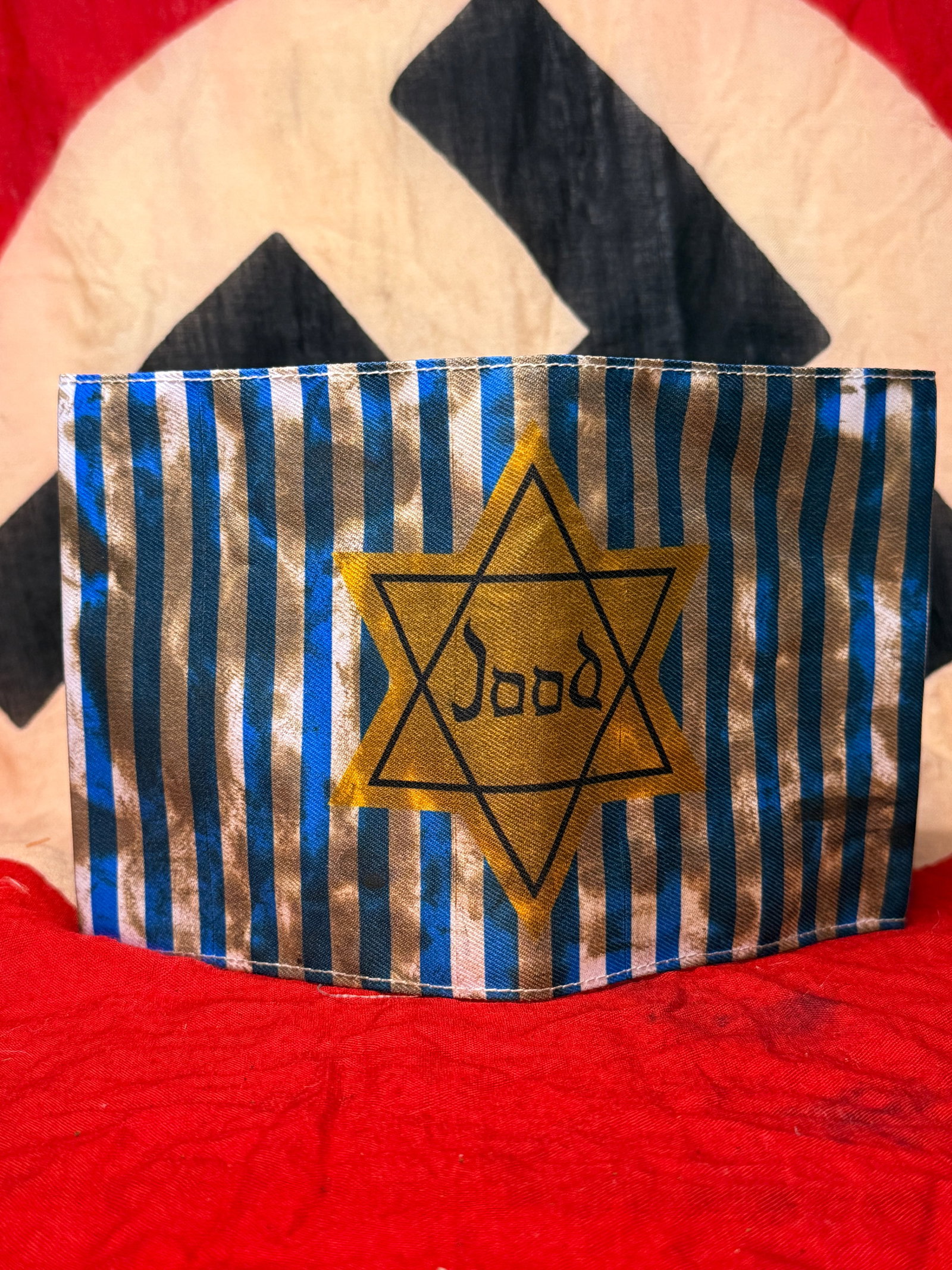 WWII German Jewish Jood Prisoner Star Armband: This cloth armband displays blue and white vertical stripes surrounding a yellow Star of David bearing the inscription "Jood," the Dutch word for "Jew." The reverse is plain with a stitched center sea
