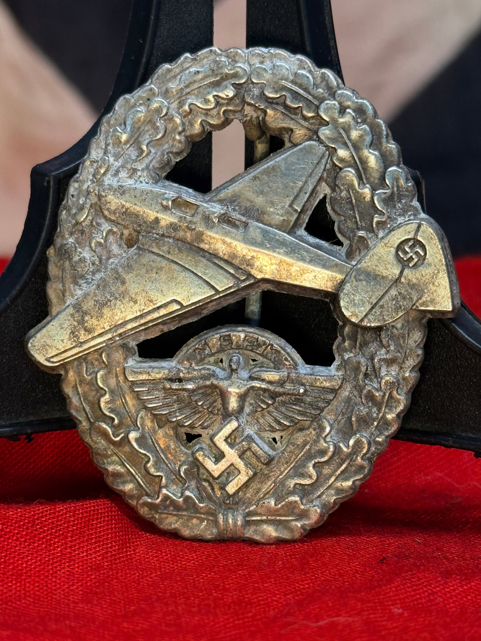 WWII German NSFK Motorized Pilot's Badge: This die-struck badge depicts a powered aircraft in flight above the NSFK eagle and swastika, all enclosed within an oak leaf wreath. The reverse retains its original pin and catch assembly, while the