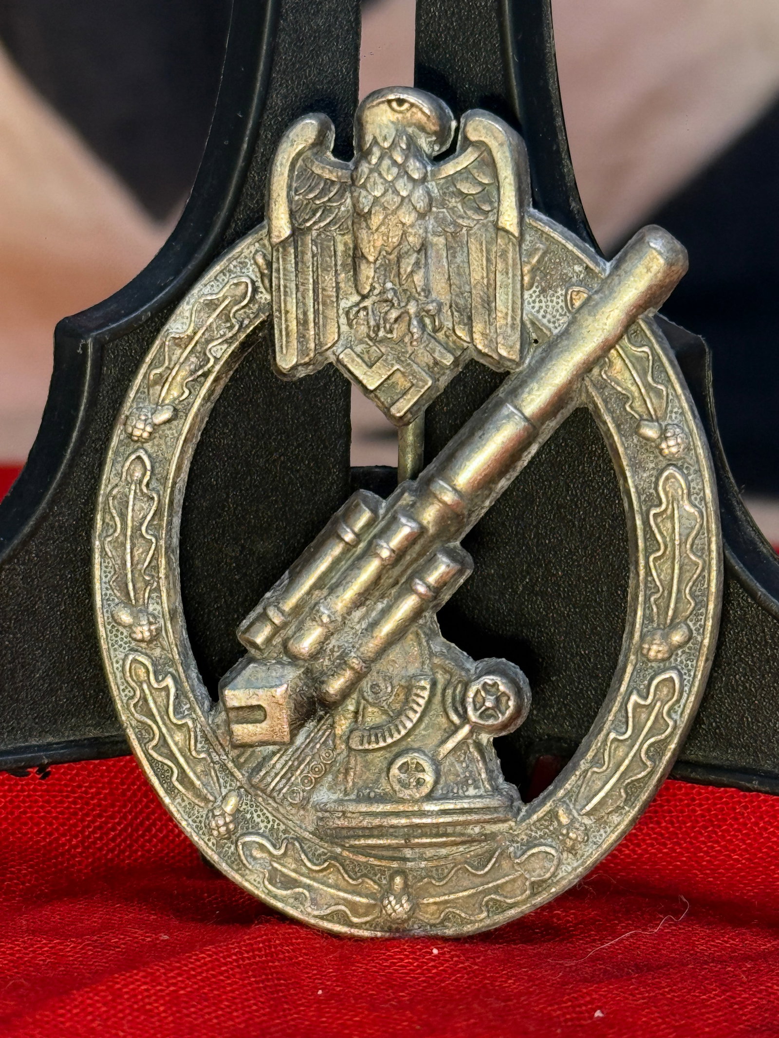 WWII German Army Anti-Aircraft Badge By WH WIEN: This silver-toned oval badge depicts a detailed anti-aircraft gun beneath the Wehrmacht eagle and swastika, enclosed within an ornate oak leaf wreath. The reverse retains its original vertical pin ass