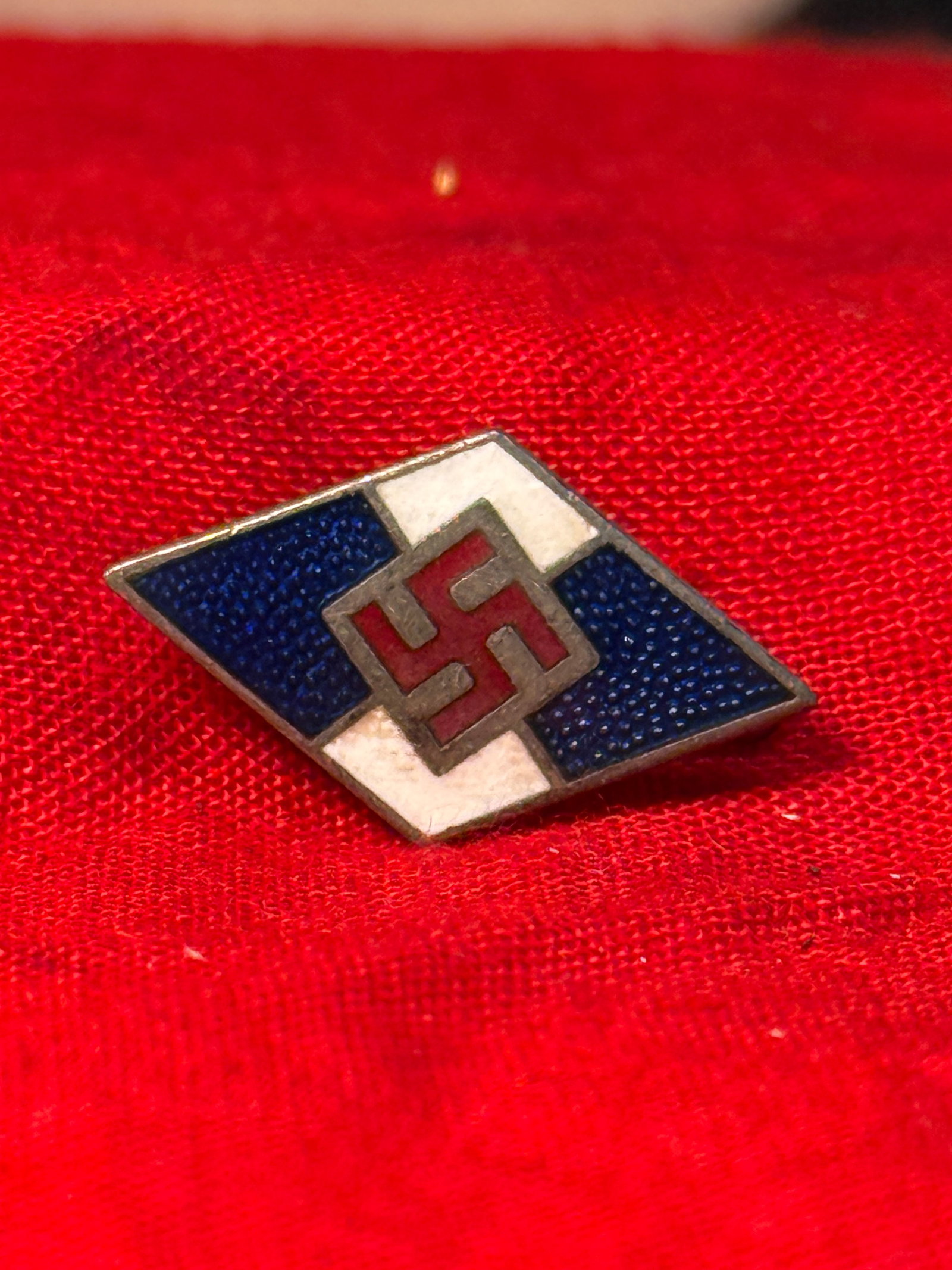 WWII German Hitler Youth Membership Badge: This enameled diamond-shaped badge displays the distinctive blue, white, and red Hitler Youth design with a central swastika. The reverse retains its original horizontal pin assembly and is maker mark