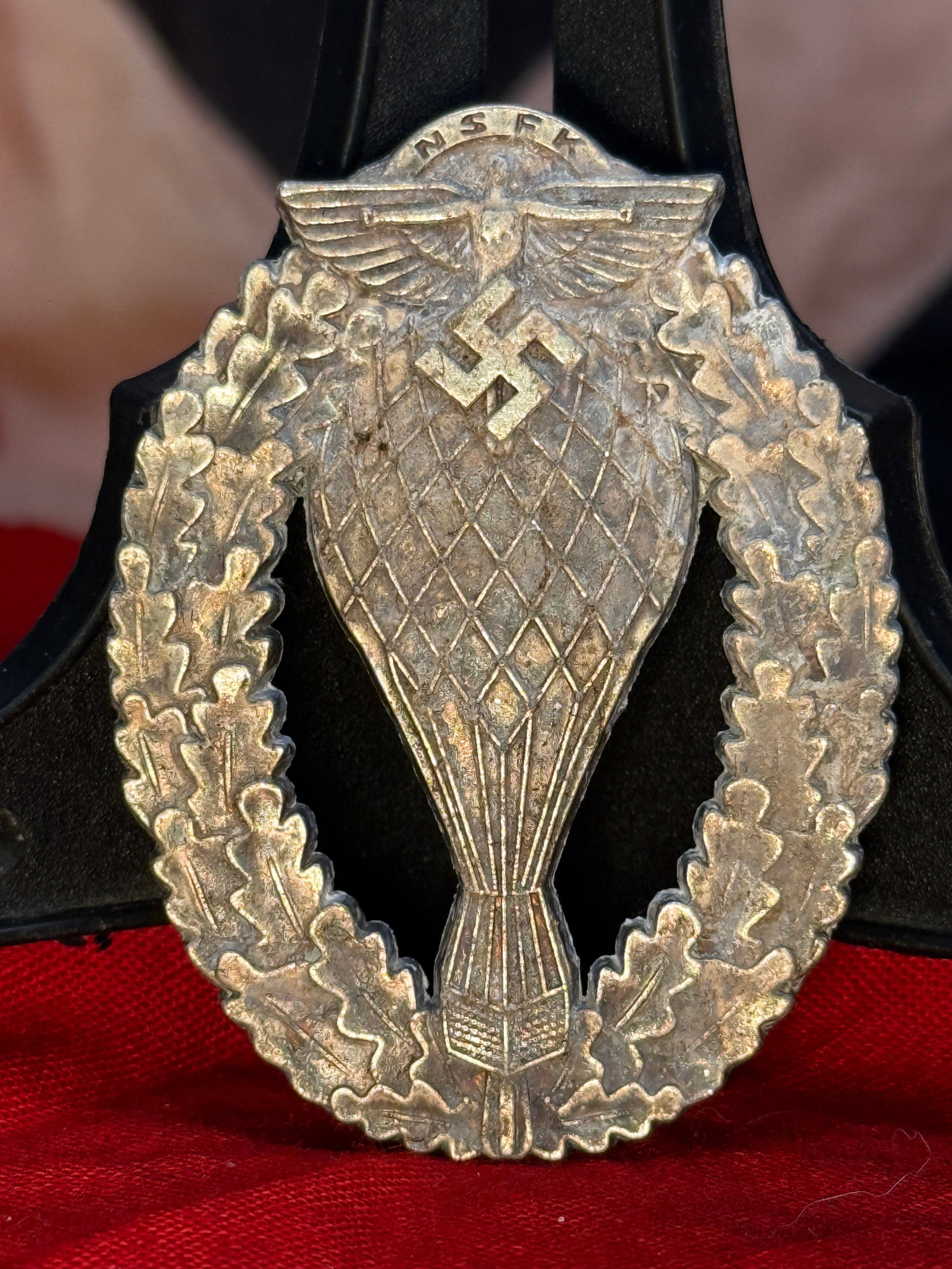 WWII German Fallschirmjäger Paratrooper Badge Serial No. 231240: This silver-toned badge depicts a diving eagle clutching a swastika over an open parachute surrounded by an oak leaf wreath. The reverse retains its original vertical pin assembly and is serial number