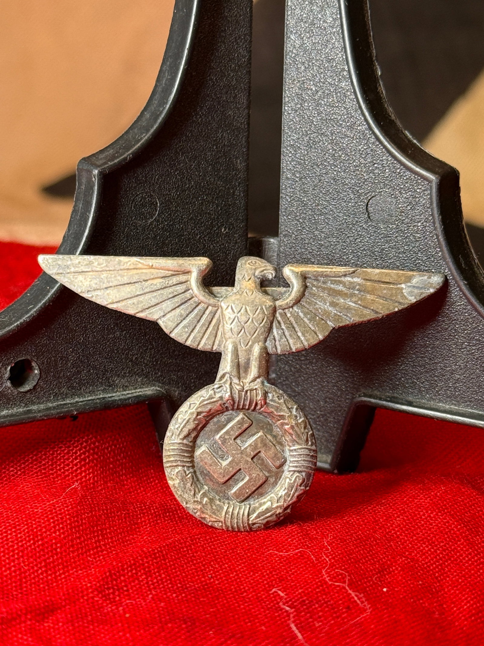 WWII German Wehrmacht Heer Cap Eagle Insignia: This WWII German Wehrmacht Heer cap eagle insignia features the national eagle with outstretched wings clutching a wreath enclosing a swastika. Constructed of die-struck metal with a horizontal pin-ba