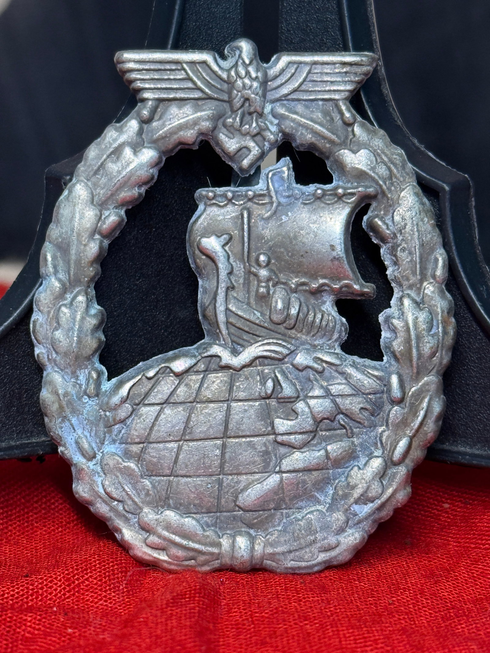 WWII German Kriegsmarine High Seas Fleet Badge: This WWII German Kriegsmarine High Seas Fleet Badge features a detailed battleship sailing across a globe enclosed within an oak leaf wreath surmounted by the national eagle clutching a swastika. Inst