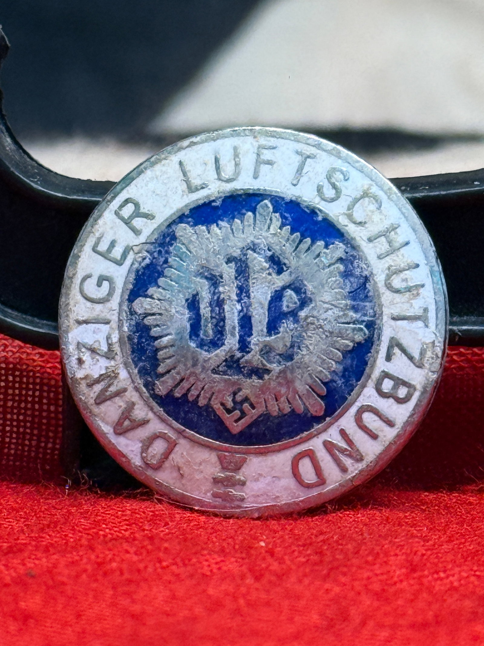 WWII German Danziger Luftschutzbund Membership Badge By RZM M1/129: This WWII German Danziger Luftschutzbund Membership Badge is a circular enameled badge bearing the inscription "DANZIGER LUFTSCHUTZBUND" surrounding the organization's emblem at the center. The revers