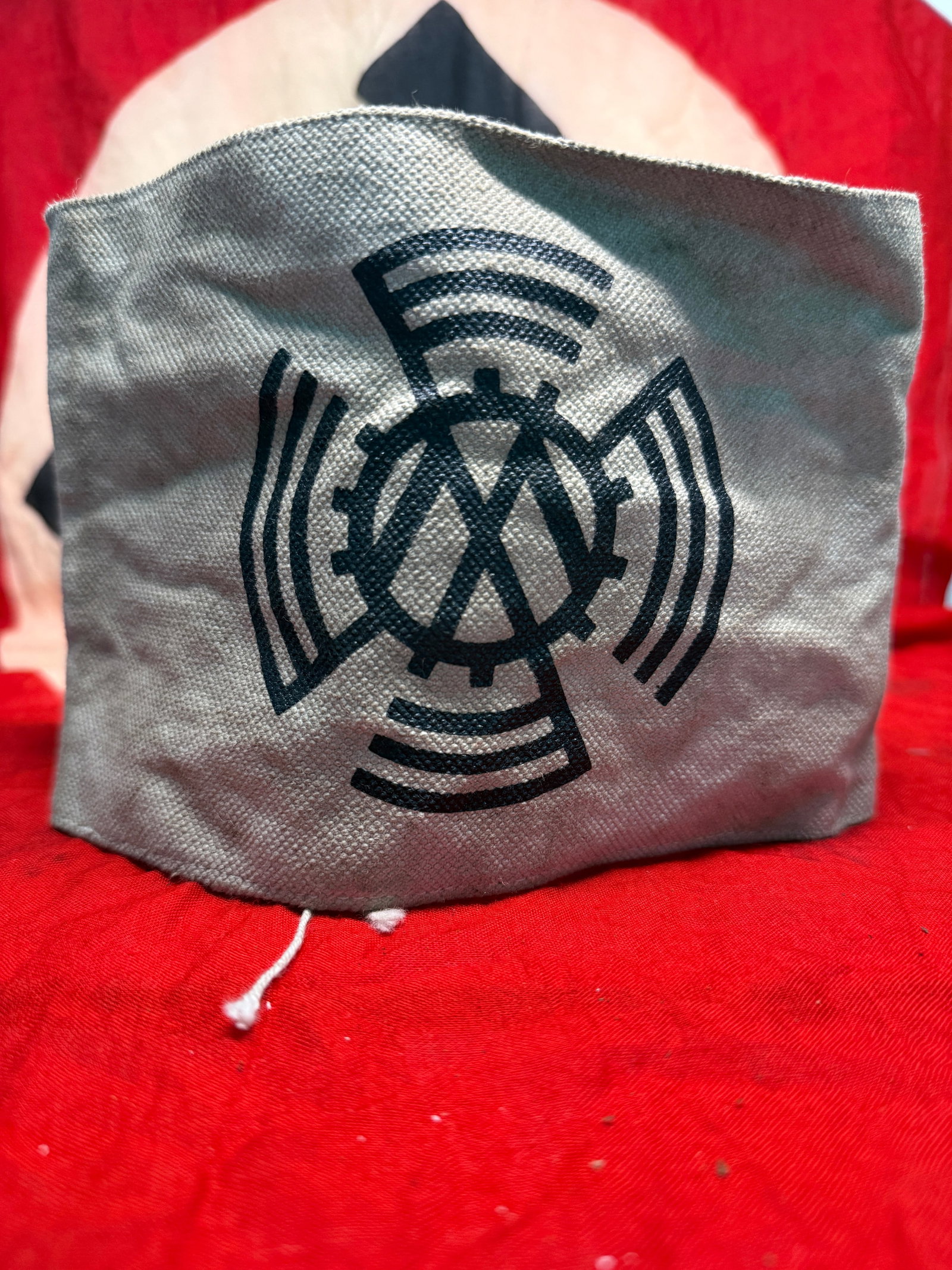 WWII German Volkswagen (KdF-Wagen) Factory Worker's Armband: This gray cloth armband features the distinctive Volkswagen emblem consisting of the interlocked "VW" monogram enclosed within a cogwheel and surrounded by stylized radiating blades, a design associat