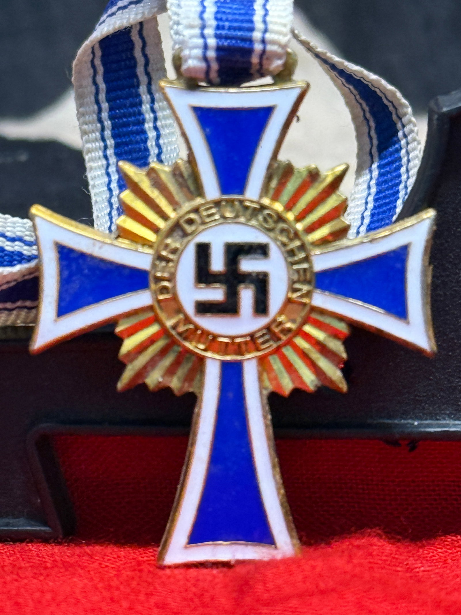 WWII German Mother's Cross Medal With Long Ribbon: This blue and white enameled cross with gilt rays and the inscription "Der Deutschen Mutter" is the Cross of Honor of the German Mother (Mutterkreuz), accompanied by its blue-and-white suspension ribb