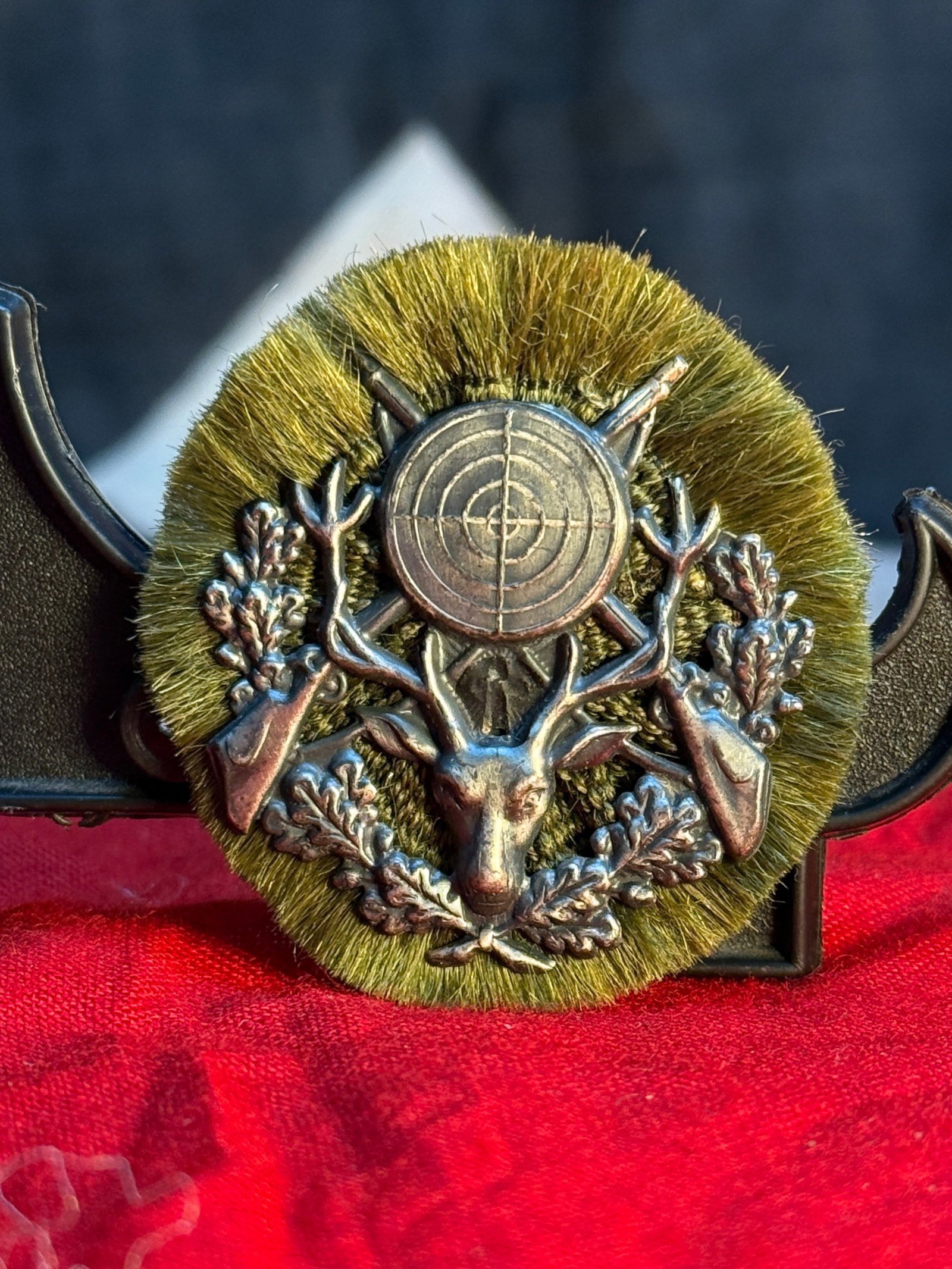 WWII German Hunting Association Marksman's Badge: This circular badge displays a stag's head beneath a target flanked by crossed rifles and oak leaves, mounted on a green simulated fur backing. The reverse retains its original pinback assembly and is