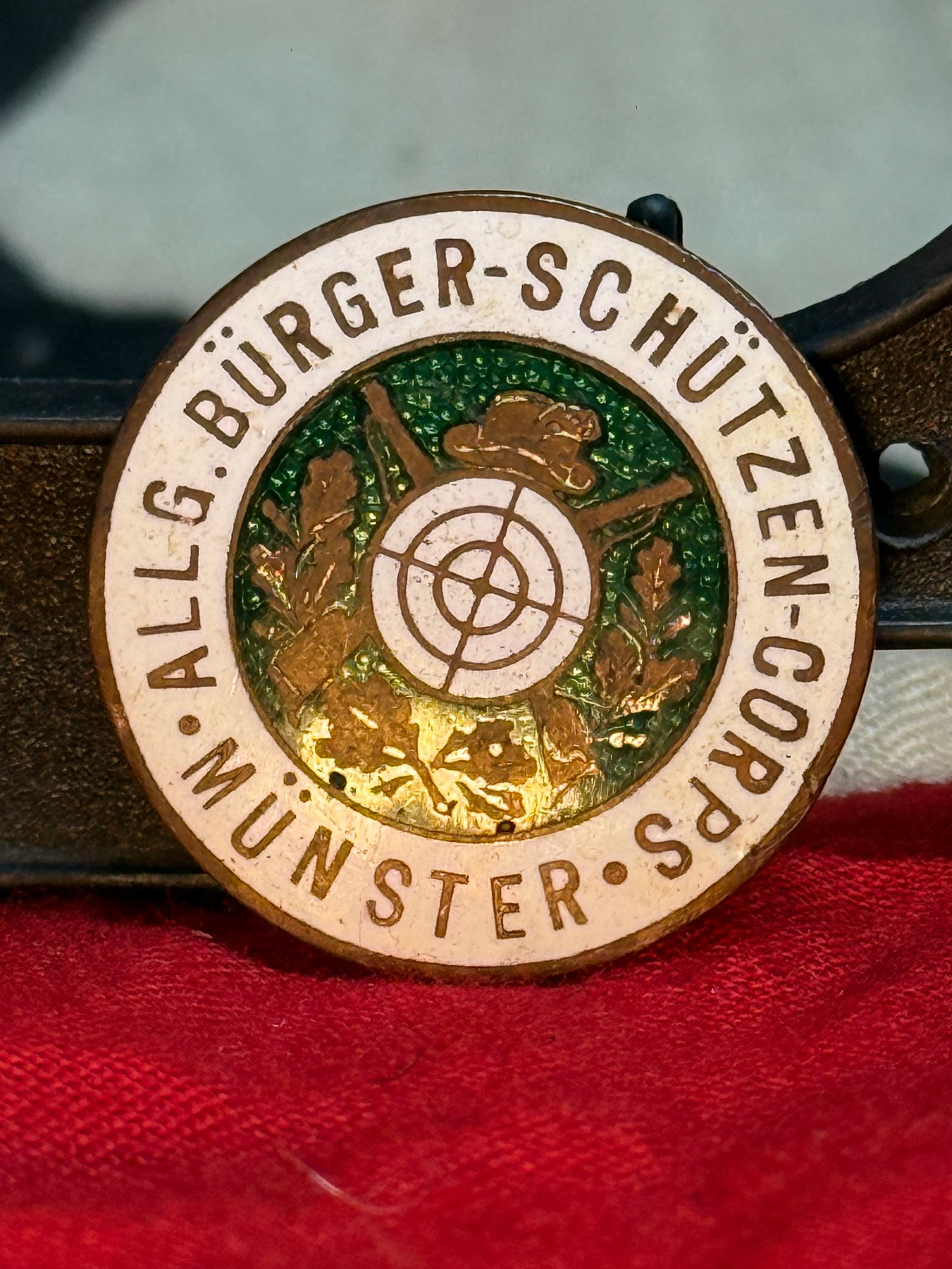 WW2 German Bürgerschützen-Corps Münster Shooting Association Badge: This enameled circular badge bears the inscription "Allg. Bürger-Schützen-Corps Münster" surrounding a target, crossed rifles, hunting hat, and oak leaves. The reverse retains its horizontal pinbac
