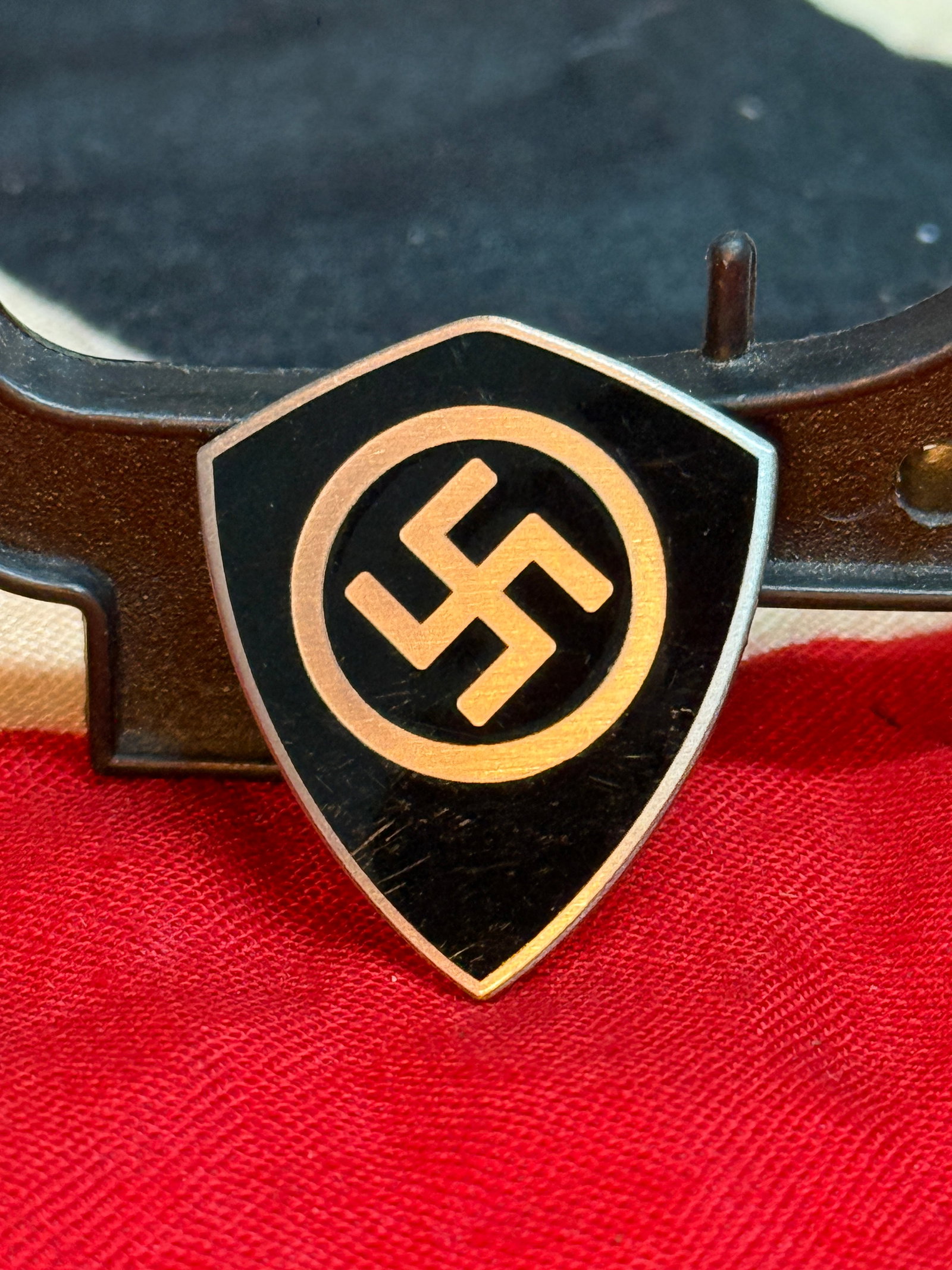 WWII German Shield-Form Political Lapel Pin By Ges. Gesch.: This shield-shaped enameled lapel pin features a black field with a white circle surrounding a red swastika, bordered by a silver-colored edge. The reverse is maker marked "GES. GESCH." and retains it