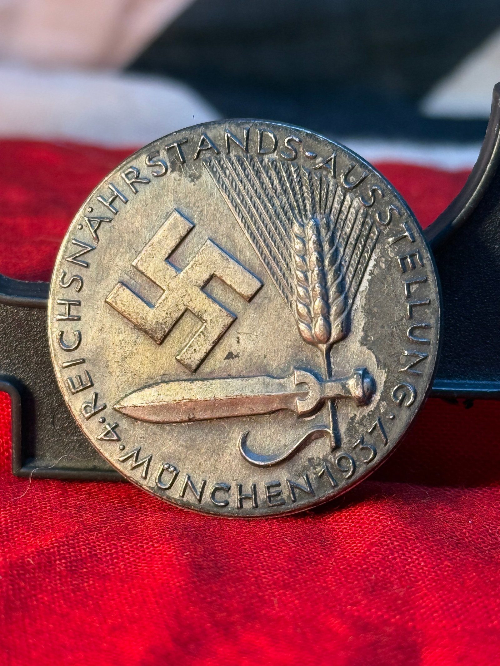 WWII German Reichsnährstand Exhibition Badge – München 1937: This bronze-toned circular badge commemorates the 1937 Reichsnährstand Exhibition held in Munich. The obverse displays a swastika, sword, sheaf of wheat, and agricultural symbols surrounded by the in