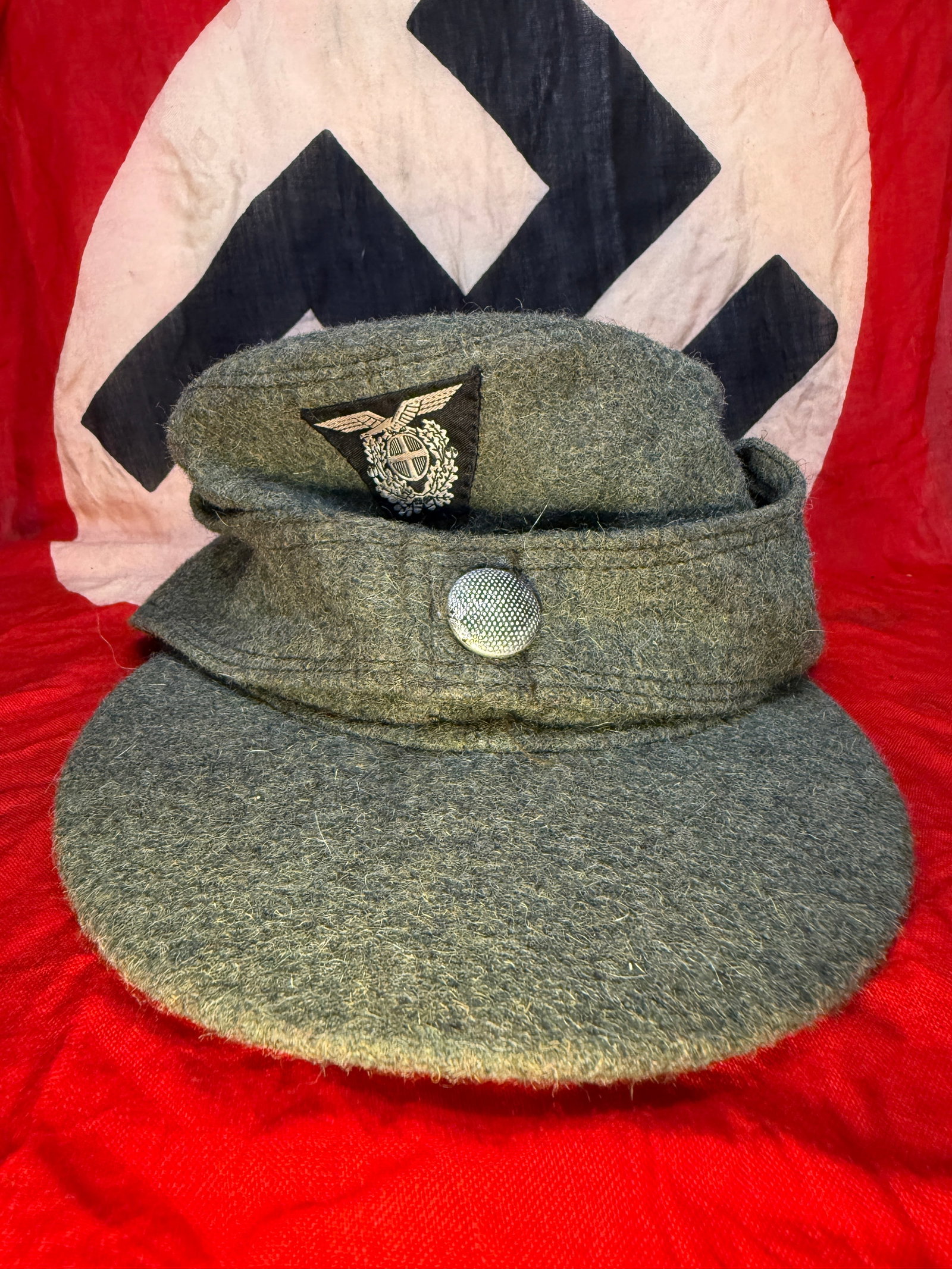 WWII German Luftwaffe Einheitsfeldmütze M43 Field Cap: This WWII German Luftwaffe Einheitsfeldmütze M43 field cap is constructed of blue-gray wool with the characteristic fold-down side panels and short visor introduced late in the war. The front retains