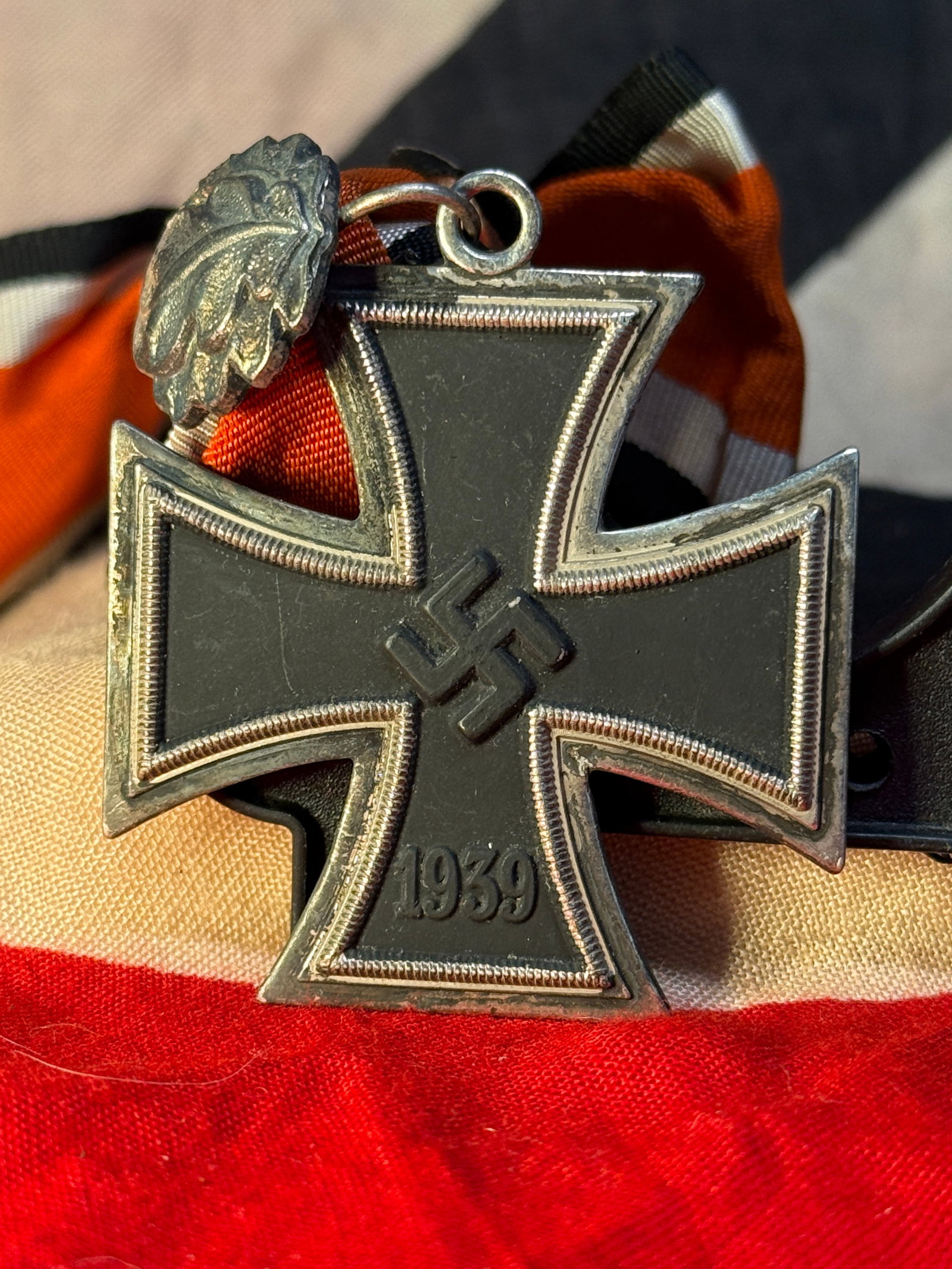WWII German Iron Cross 2nd Class 1939 with Ribbon: This WWII German Iron Cross 2nd Class (Eisernes Kreuz 2. Klasse 1939) retains its original black, white, and red suspension ribbon together with the medal. The obverse displays the swastika above the 