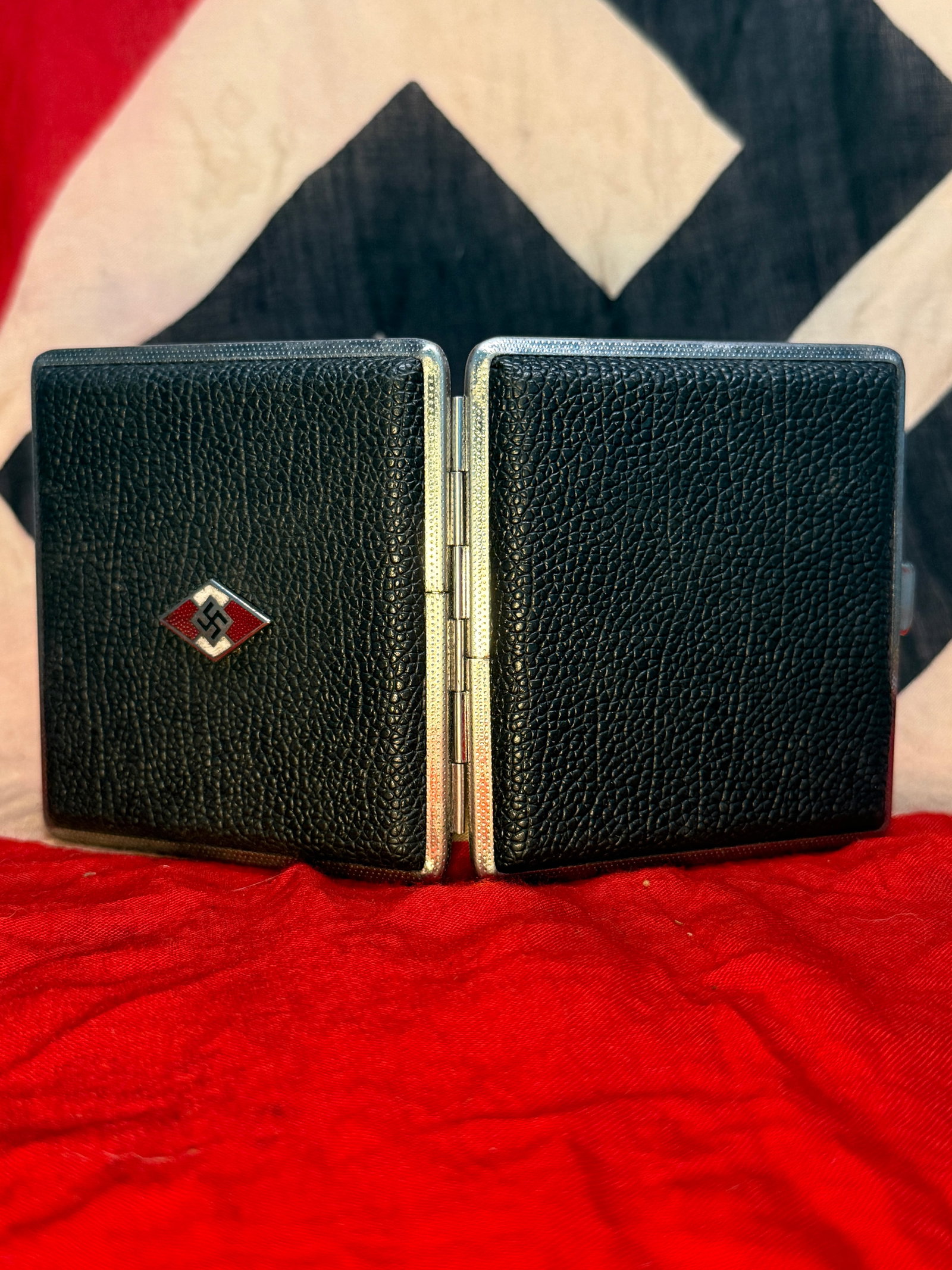 WWII German Hitler Youth HJ Cigarette Case Black Textured Finish Enamel Emblem: WWII German Hitler Youth cigarette case featuring a black textured exterior, silver-tone metal edging, and a red, white, and black diamond-shaped HJ emblem with swastika on the front. The hinged case 