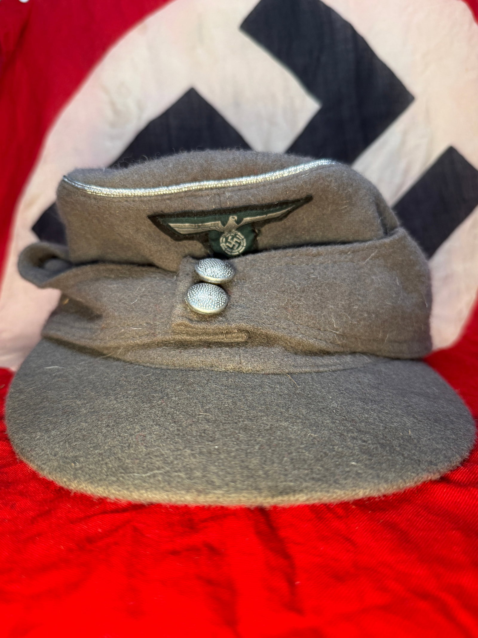 WWII German Wehrmacht Heer M43 Field Cap: This WWII German Wehrmacht Heer M43 field cap is constructed of field-gray wool and features the distinctive fold-down side panels secured by two pebbled aluminum buttons. The front displays a machine