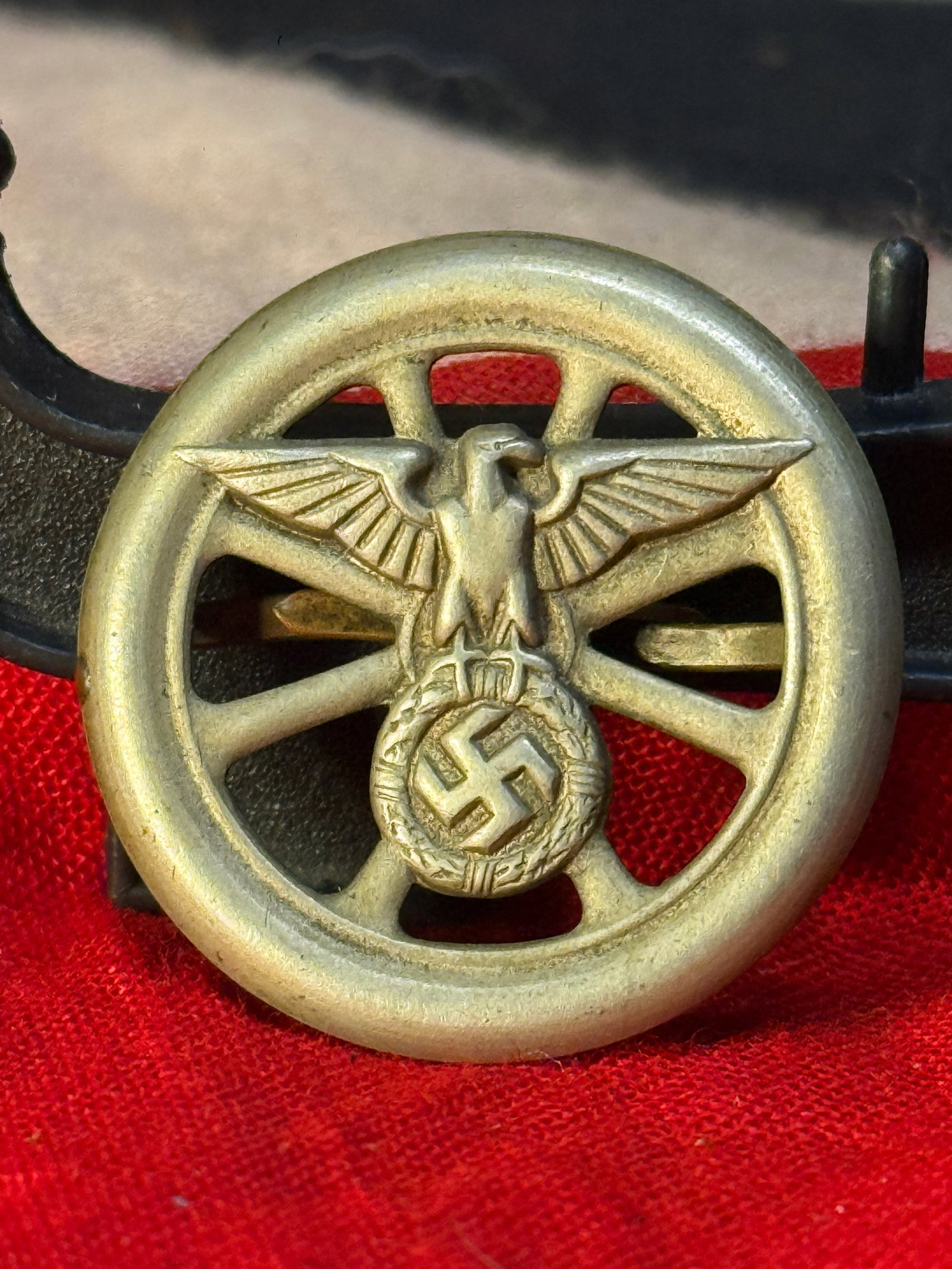 WWII German Reichsautobahn Cap Badge: This WWII German Reichsautobahn cap badge features an openwork wheel surmounted by the national eagle grasping a wreath enclosing the swastika. Constructed in bronze-colored metal, the badge retains i