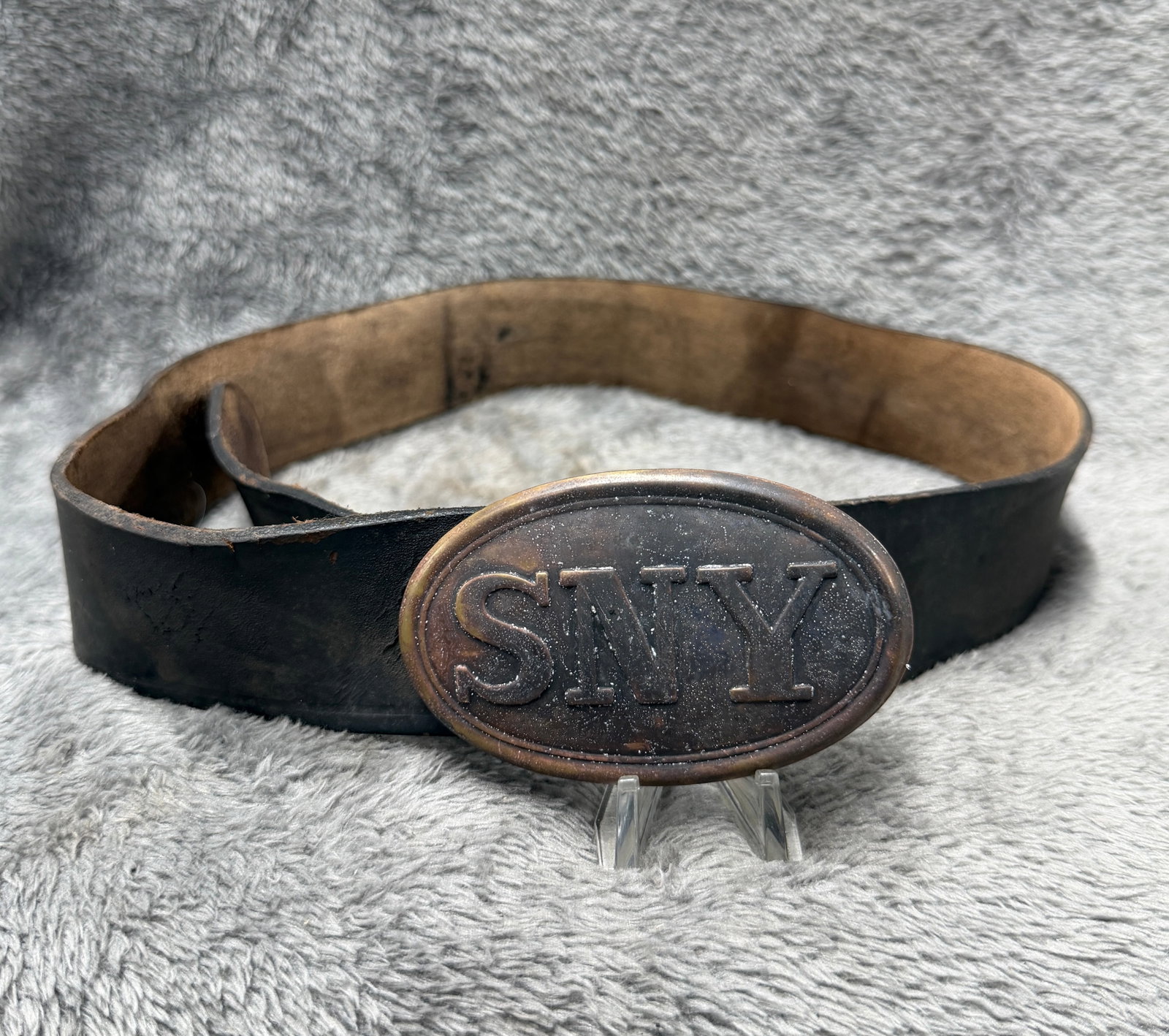 Civil War New York SNY State Militia Oval Belt Buckle Plate with Leather Belt: Offered is an oval metal belt plate featuring large raised “SNY” lettering within a double-line oval border, accompanied by a wide black leather belt. The plate has a dark aged surface with br