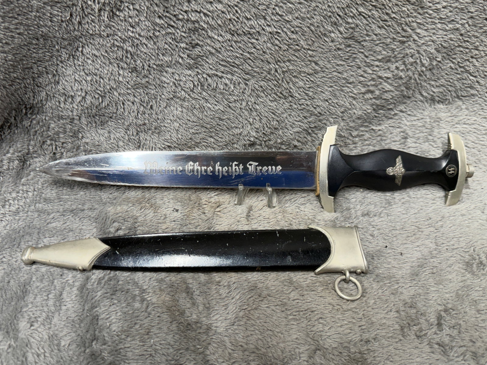 WWII German Waffen SS Dagger with Scabbard – “Meine Ehre heißt Treue?? Inscription – RZM: Offered is a German SS-style dagger with matching black scabbard, measuring approximately 13½–14 inches overall based on the photograph provided. The dagger features a black contoured grip fi