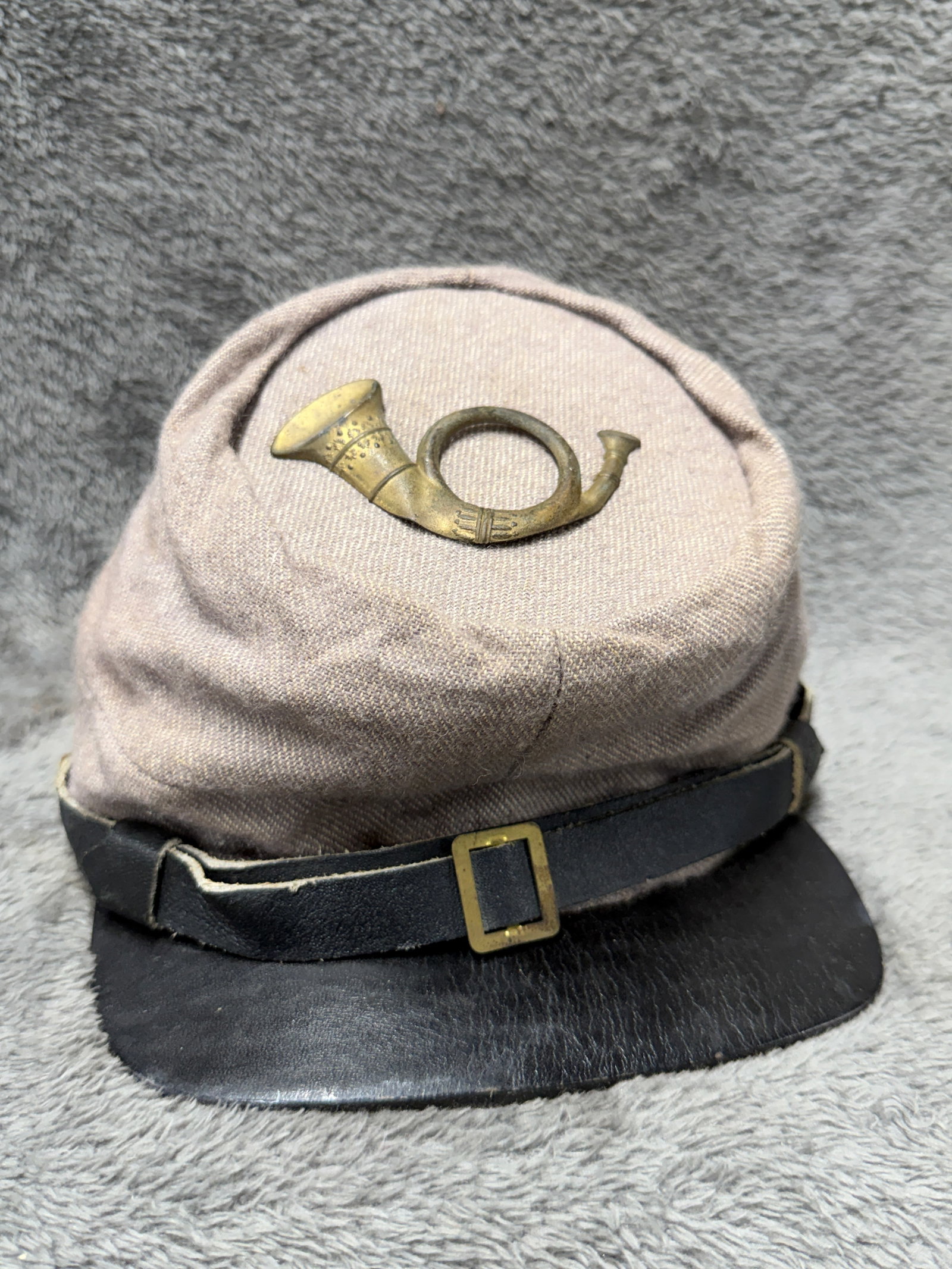 Civil War Style Confederate Artillery Kepi Cap with Brass Bugle Insignia & Leather Visor: Civil War-style military kepi featuring a gray/taupe wool-blend body, black leather visor, black leather front strap with brass-tone rectangular buckle, and brass-tone side buttons. A prominent brass 