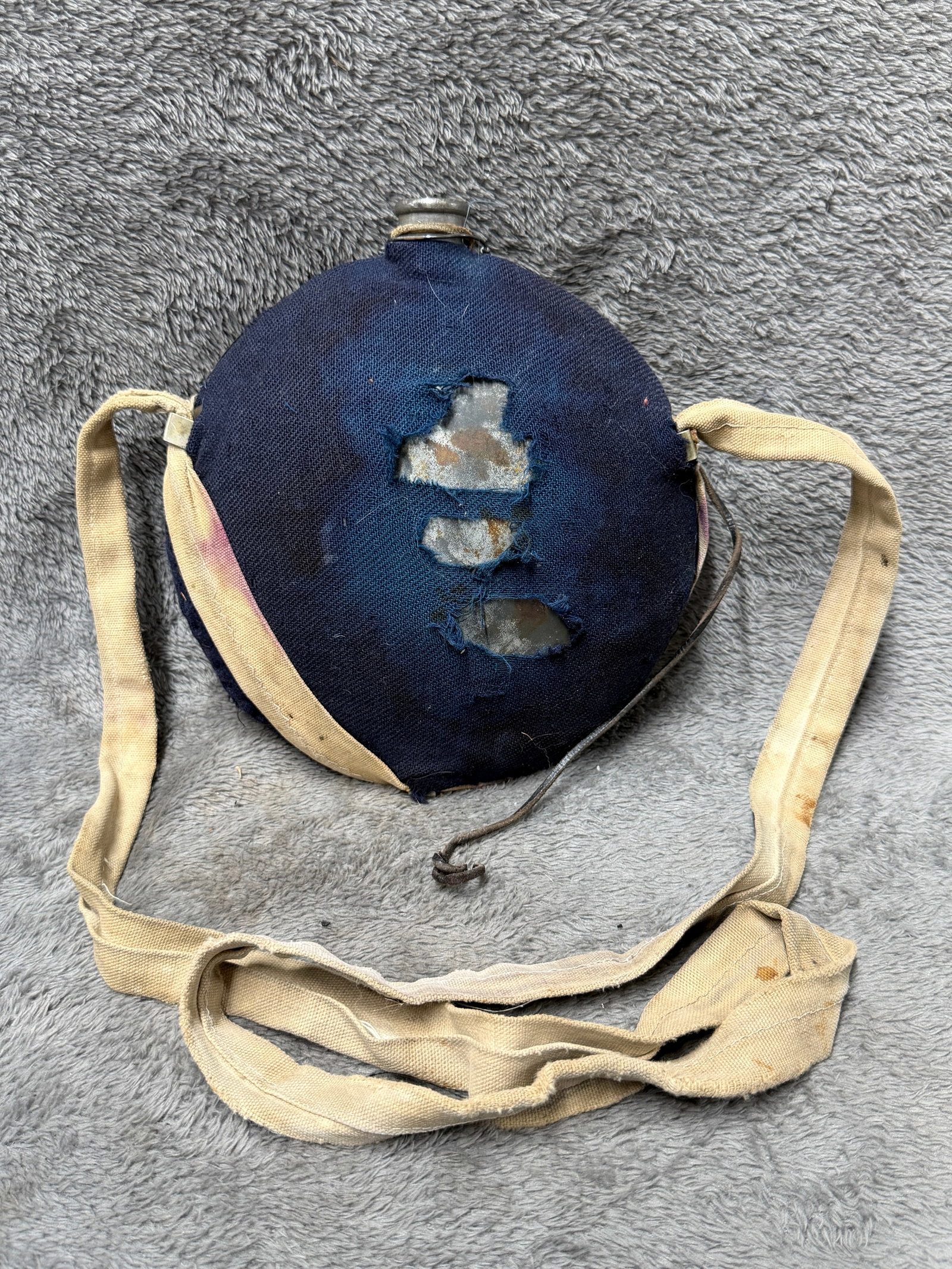 Civil War Era Military Canteen Round Metal Flask Blue Wool Cover Canvas Strap c. 1861–1865: Antique round metal military canteen featuring a dark blue cloth covering, long beige canvas shoulder strap, leather retaining straps, and a short metal drinking spout. The canteen measures approximat
