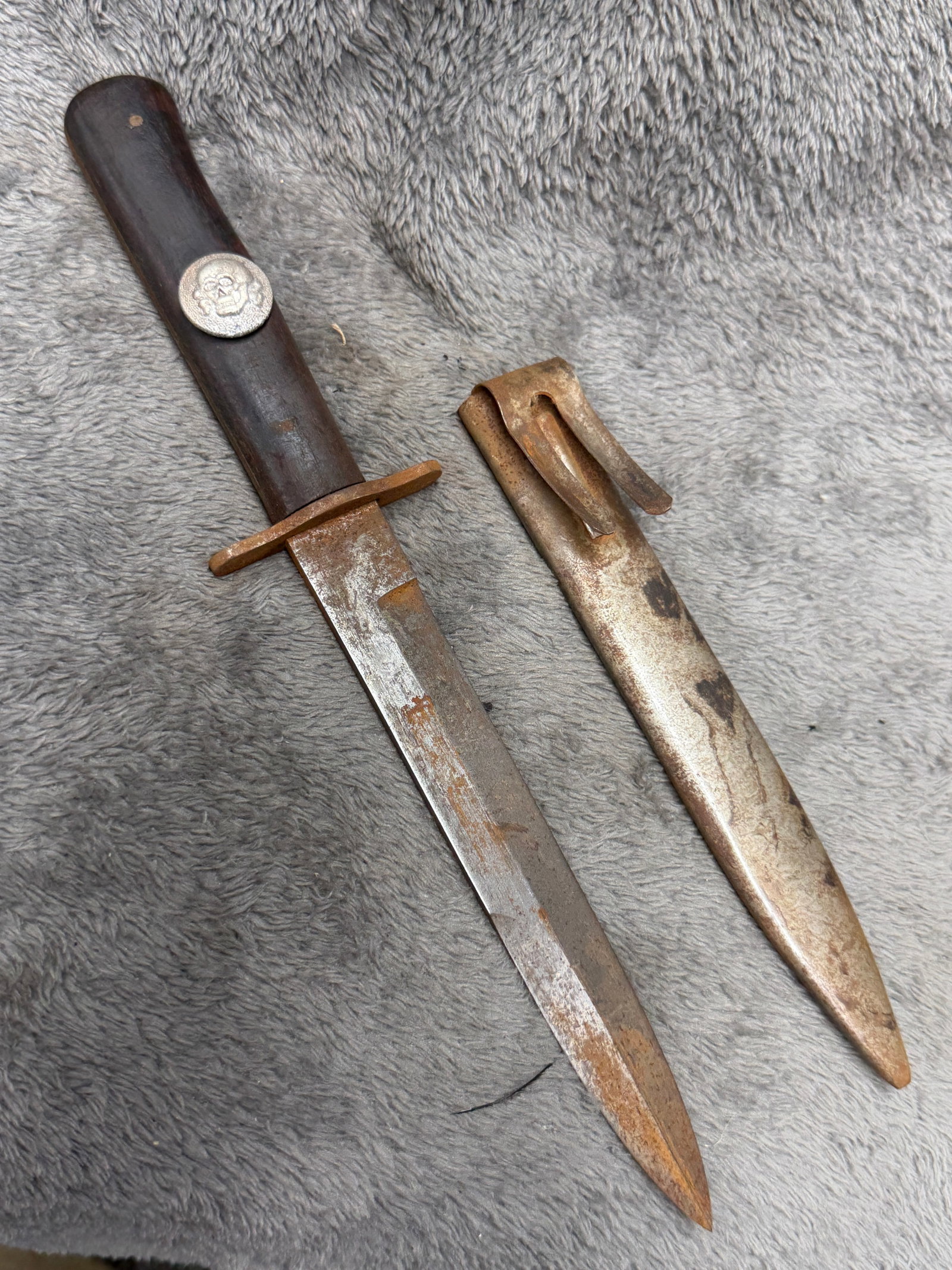 WWII German Totenkopf SS Officer Style Boot Knife with Metal Sheath: WWII German-style boot knife featuring a dark wooden grip fitted with a prominent metal Totenkopf skull emblem, simple metal crossguard, single-edged pointed blade, and fitted metal sheath with integr